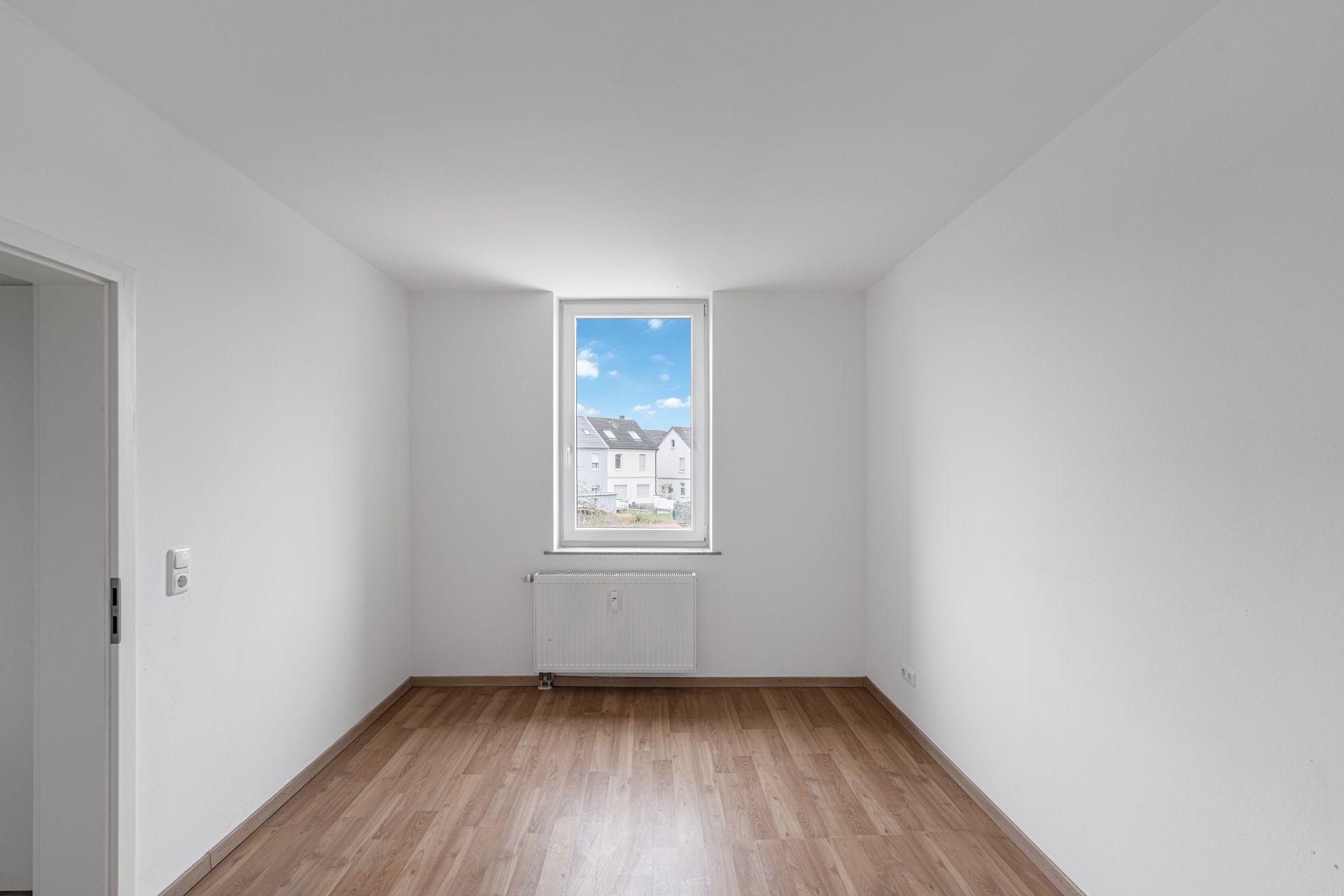 Leeres Zimmer mit weiß gestrichenen Wänden, Fenster und Holzfußboden.