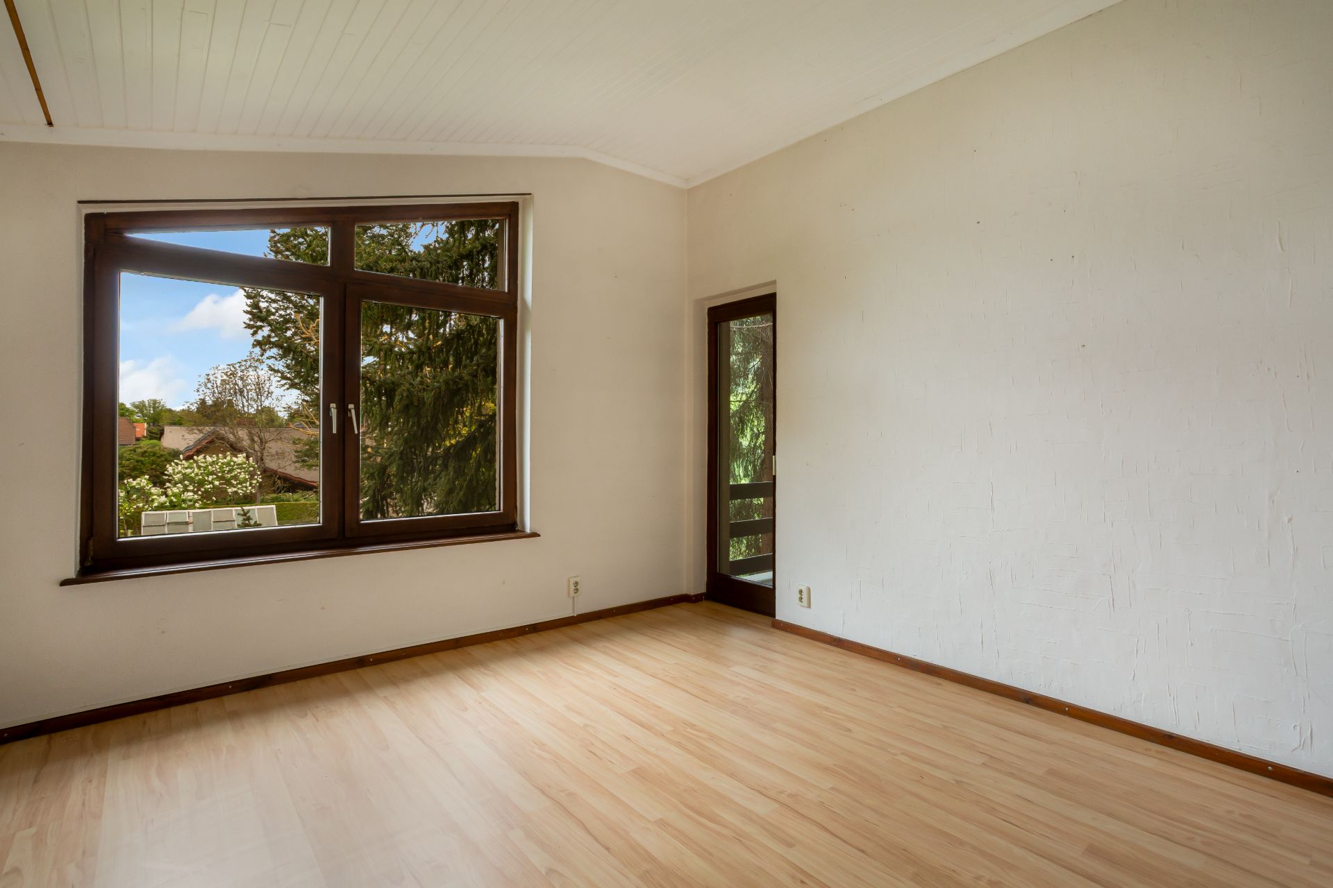 Leerer Raum mit großem Fenster, Holzboden und Tür zu einem Balkon.