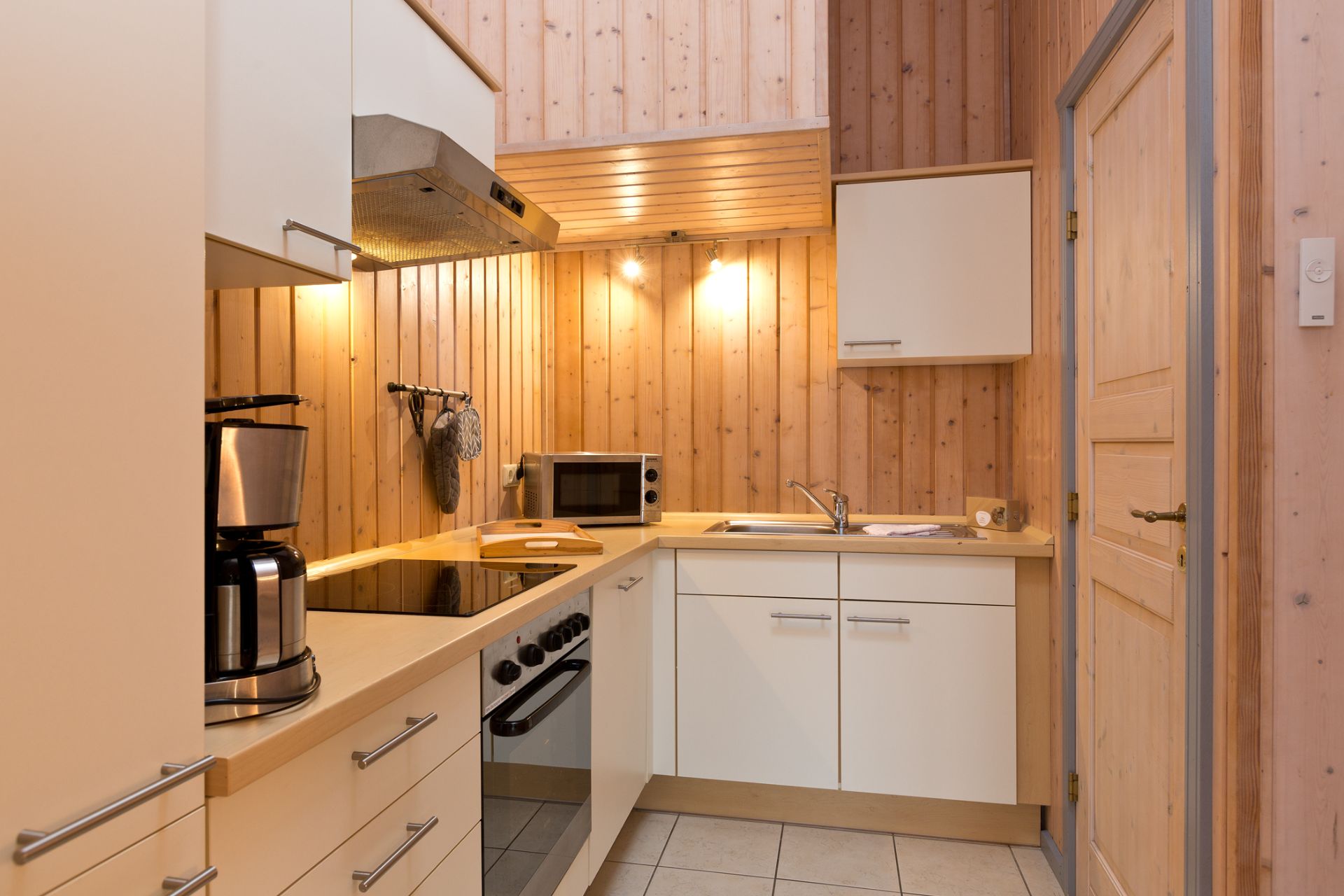 Moderne Einbauküche mit Holzverkleidung, Elektroherd, Kaffeemaschine, Mikrowelle und Spüle.
