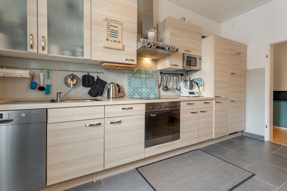 Moderne Einbauküche mit Elektrogeräten, Spüle, Herd, Backofen und Küchenutensilien an der Wand.