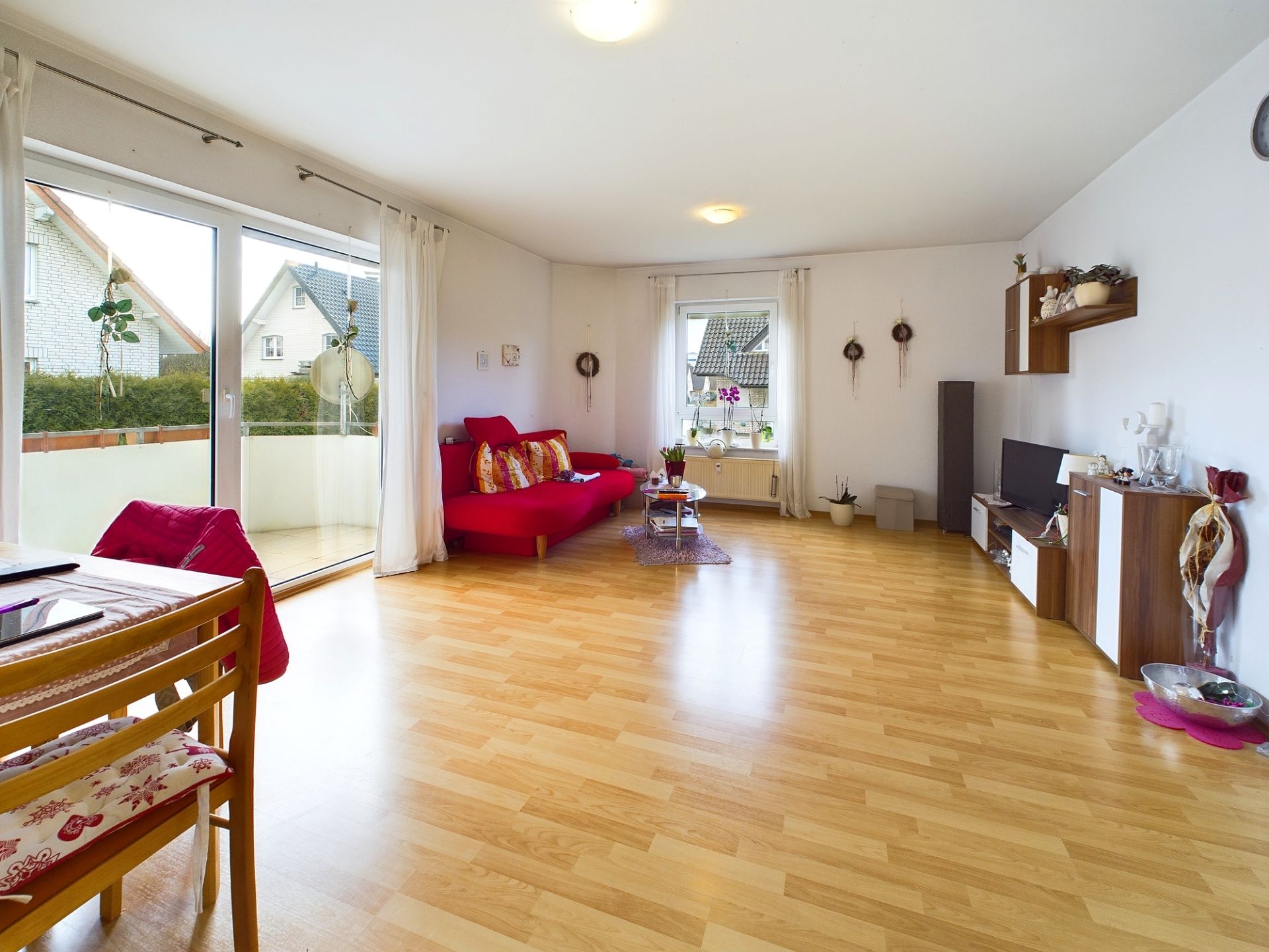 Helles Wohnzimmer mit Holzfußboden, rotem Sofa, Esstisch und bodentiefen Fenstern.