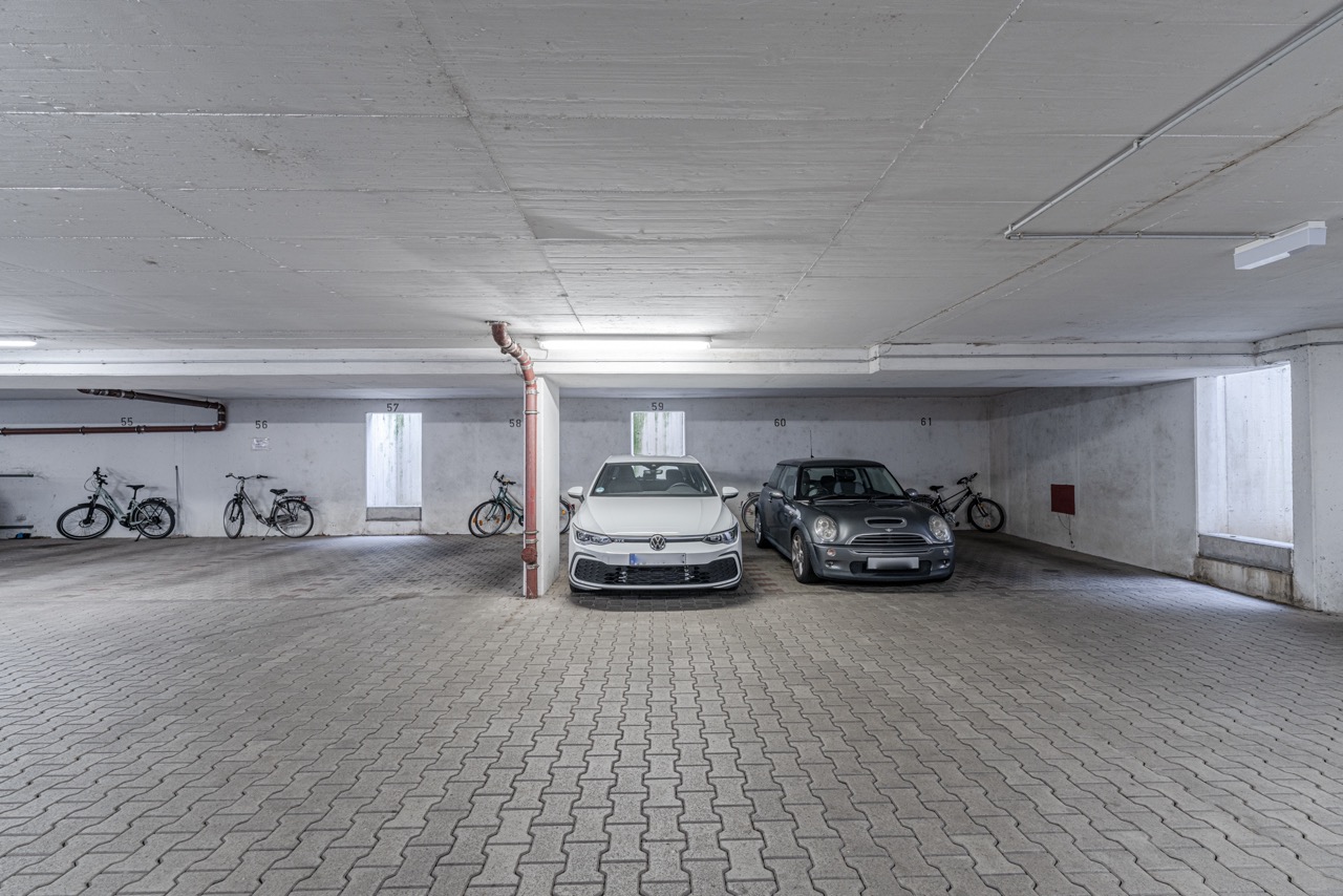 Tiefgarage mit zwei geparkten Autos und mehreren Fahrrädern an den Wänden.