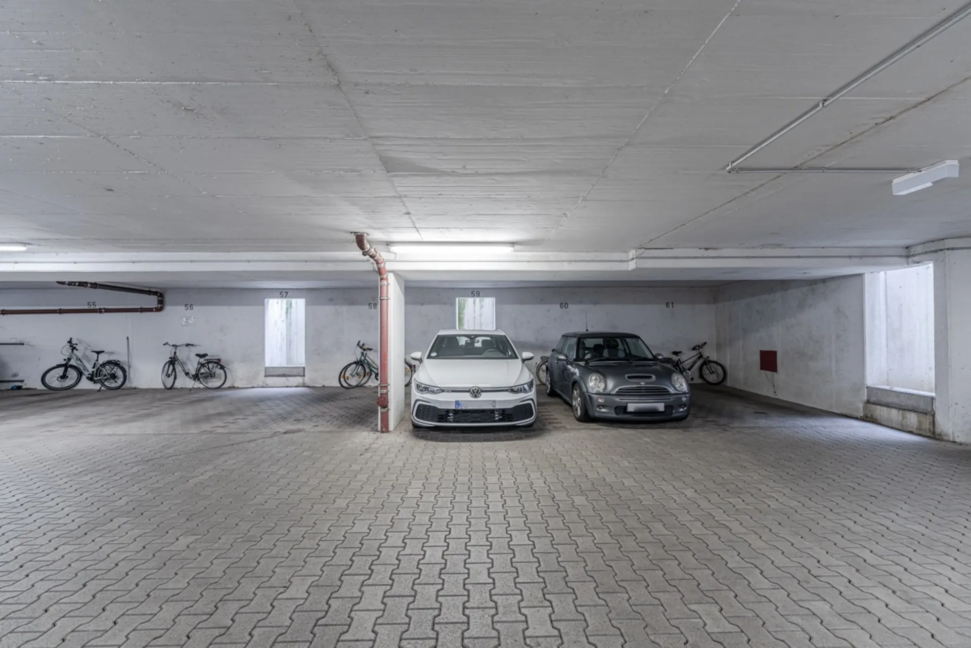 Tiefgarage mit zwei geparkten Autos und mehreren Fahrrädern an den Wänden.