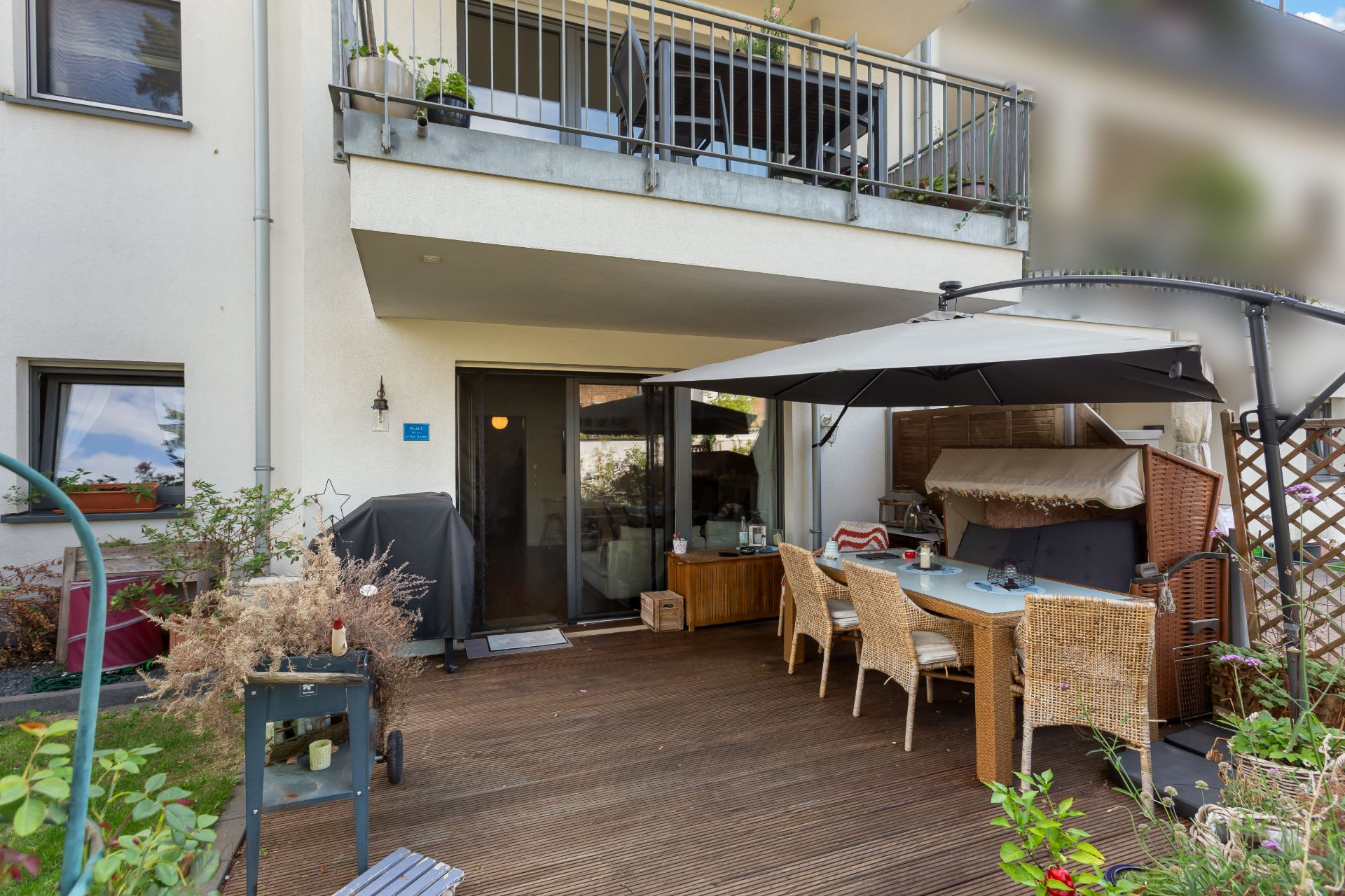 Überdachte Terrasse mit Esstisch, Stühlen und Pflanzen an einer Wohnung.