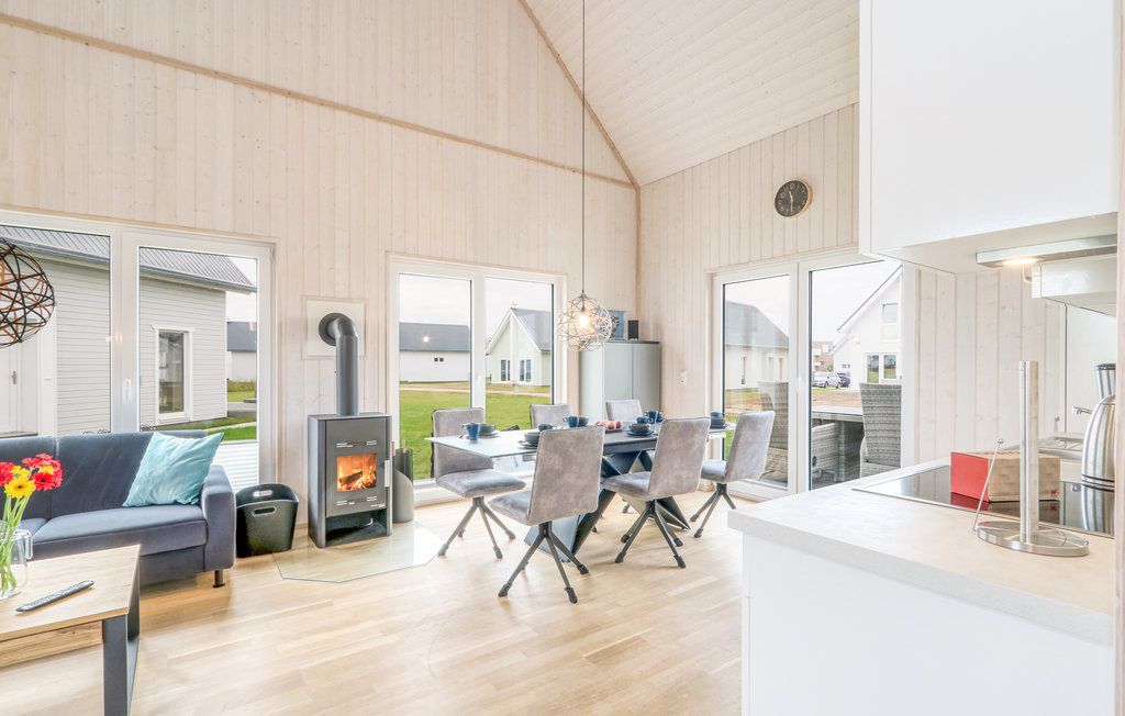 Helles Wohnzimmer mit Holzofen, Sofa, Esstisch und großen Fenstern mit Blick nach draußen.