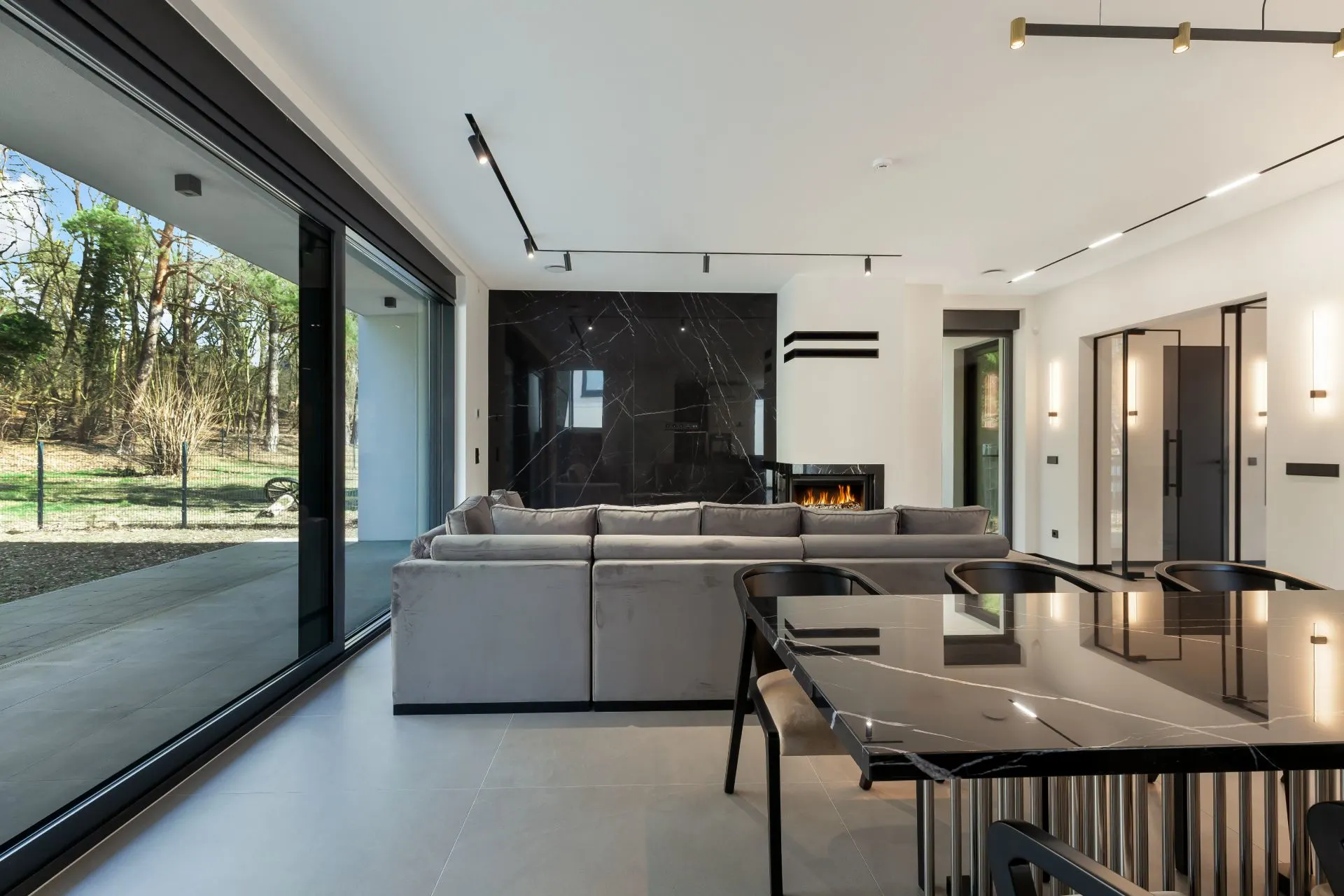 Modernes Wohnzimmer mit grauem Sofa, großem Fenster, Kamin und Esstisch aus Glas.
