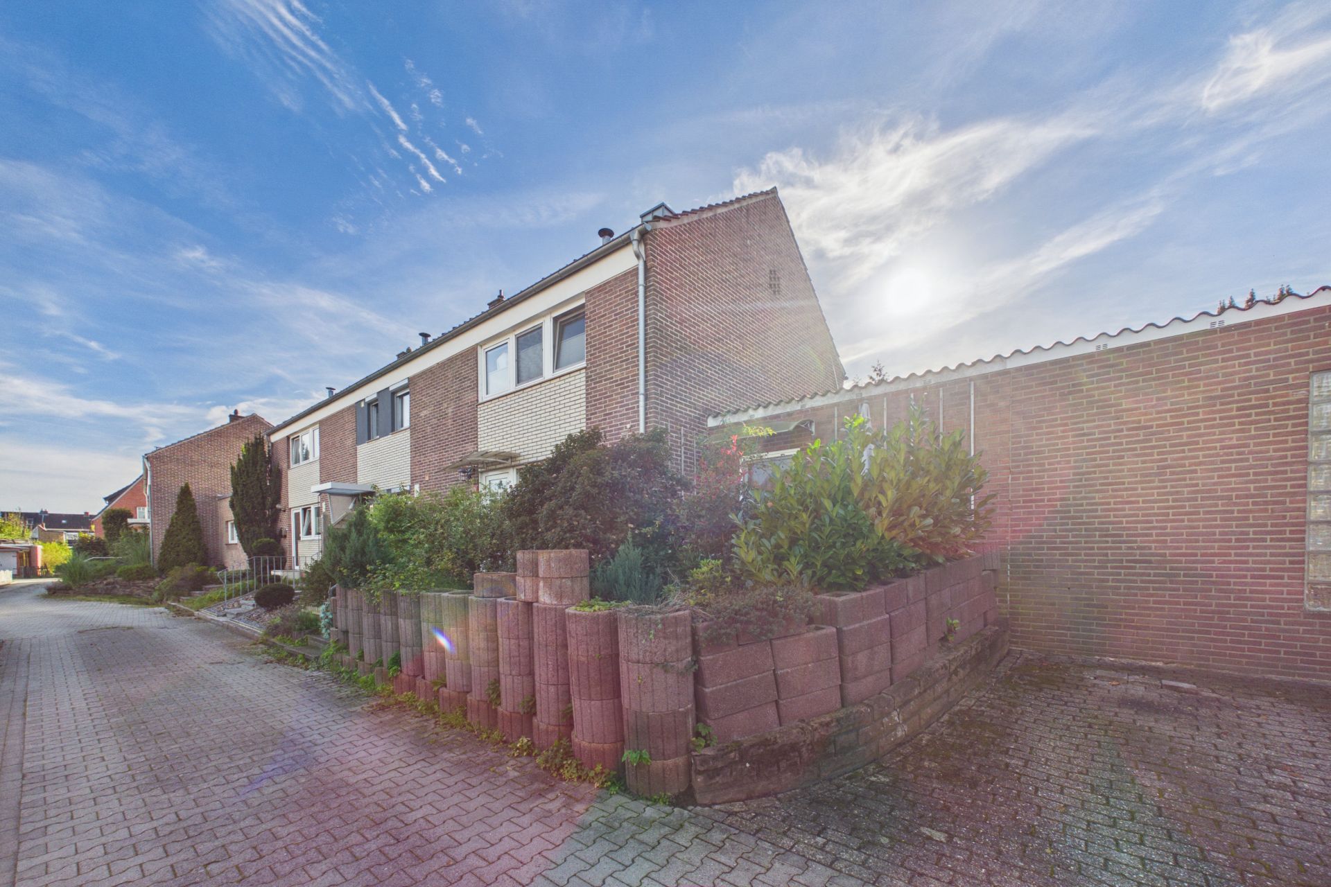 Reihenhaus mit Vorgarten und Pflasterweg bei sonnigem Wetter.