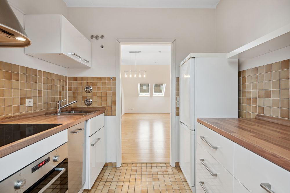 Helle Küche mit braunen Fliesen, weißen Schränken und Blick in ein Wohnzimmer mit Parkettboden.