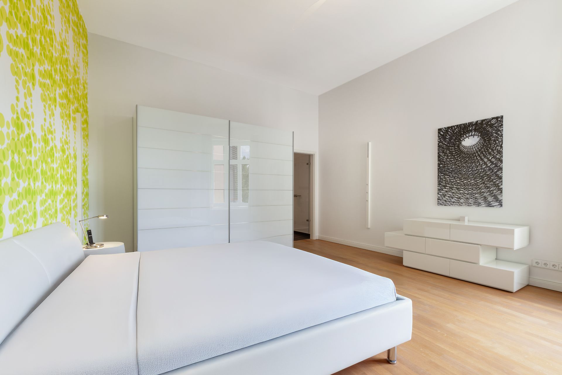 Modernes Schlafzimmer mit weißem Bett, großem Kleiderschrank und gelb gemusterter Wand.