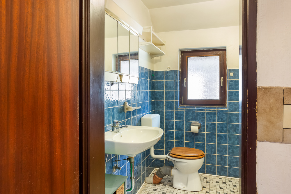 Kleines Badezimmer mit blau gefliester Wand, Waschbecken, Toilette und Fenster.