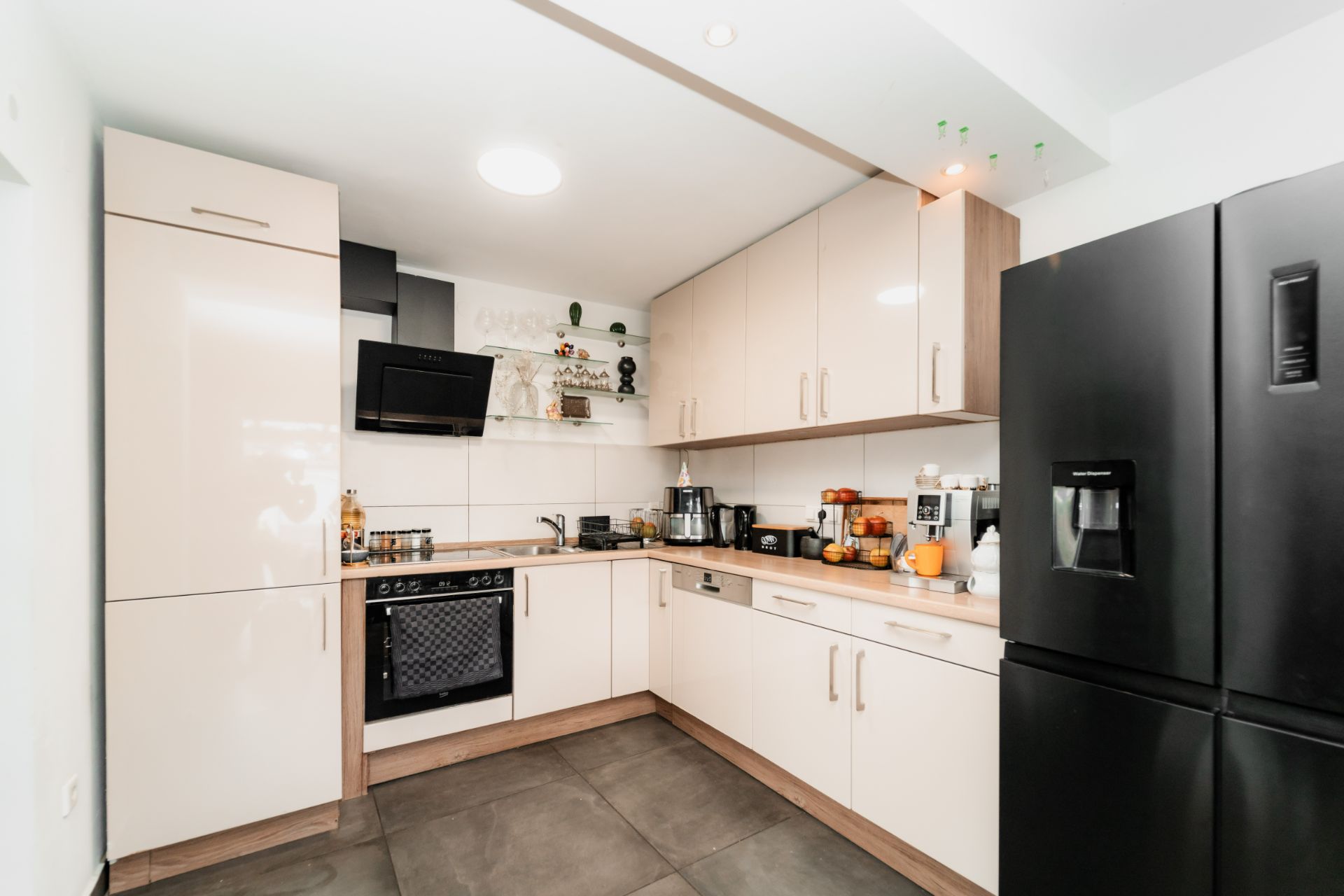 Moderne Küche mit hellen Schränken, schwarzem Kühlschrank und Einbaugeräten in L-Form.