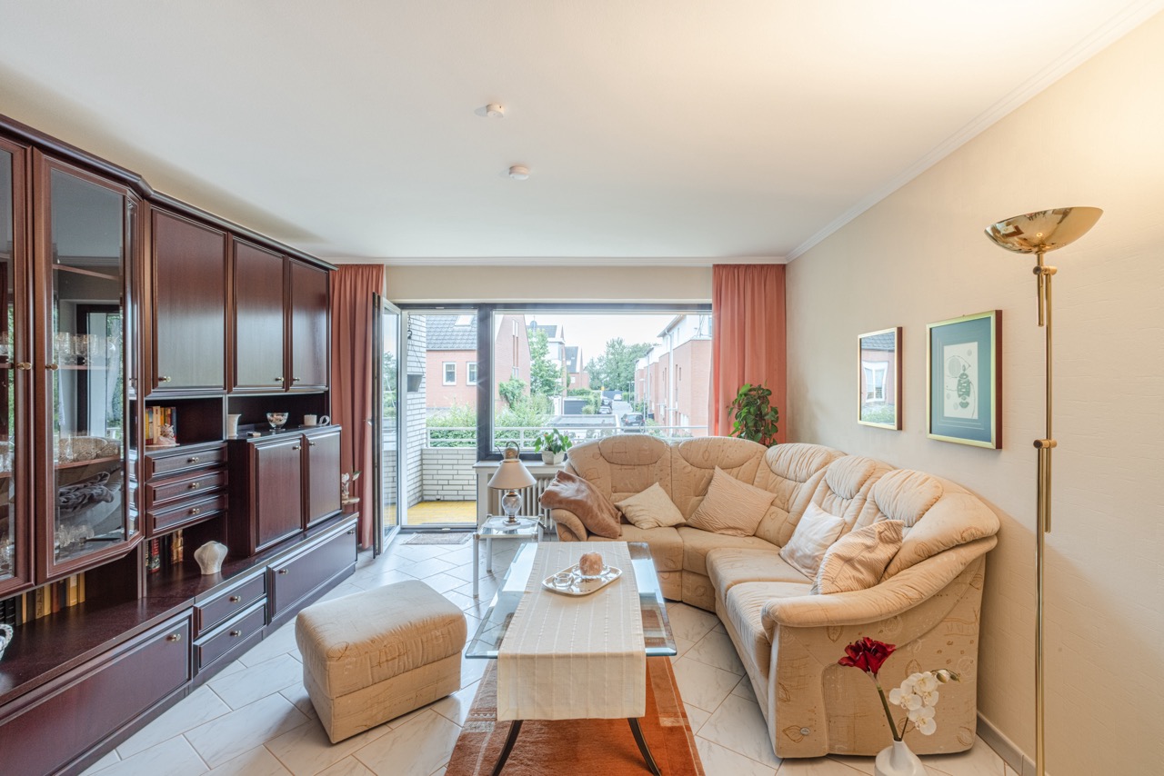Wohnzimmer mit Ecksofa, Glastisch, Schrankwand und Zugang zum Balkon.