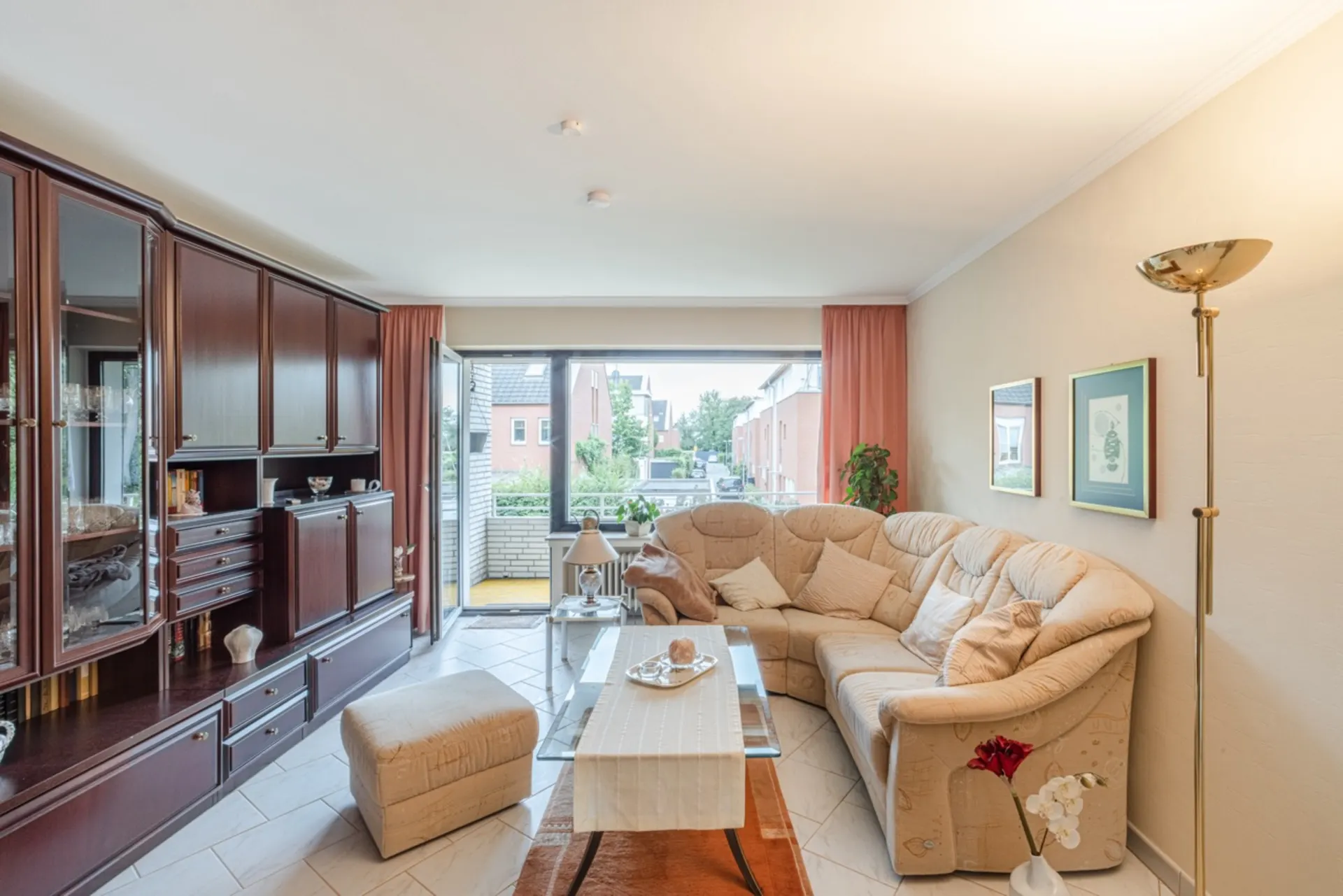 Wohnzimmer mit Ecksofa, Glastisch, Schrankwand und Zugang zum Balkon.