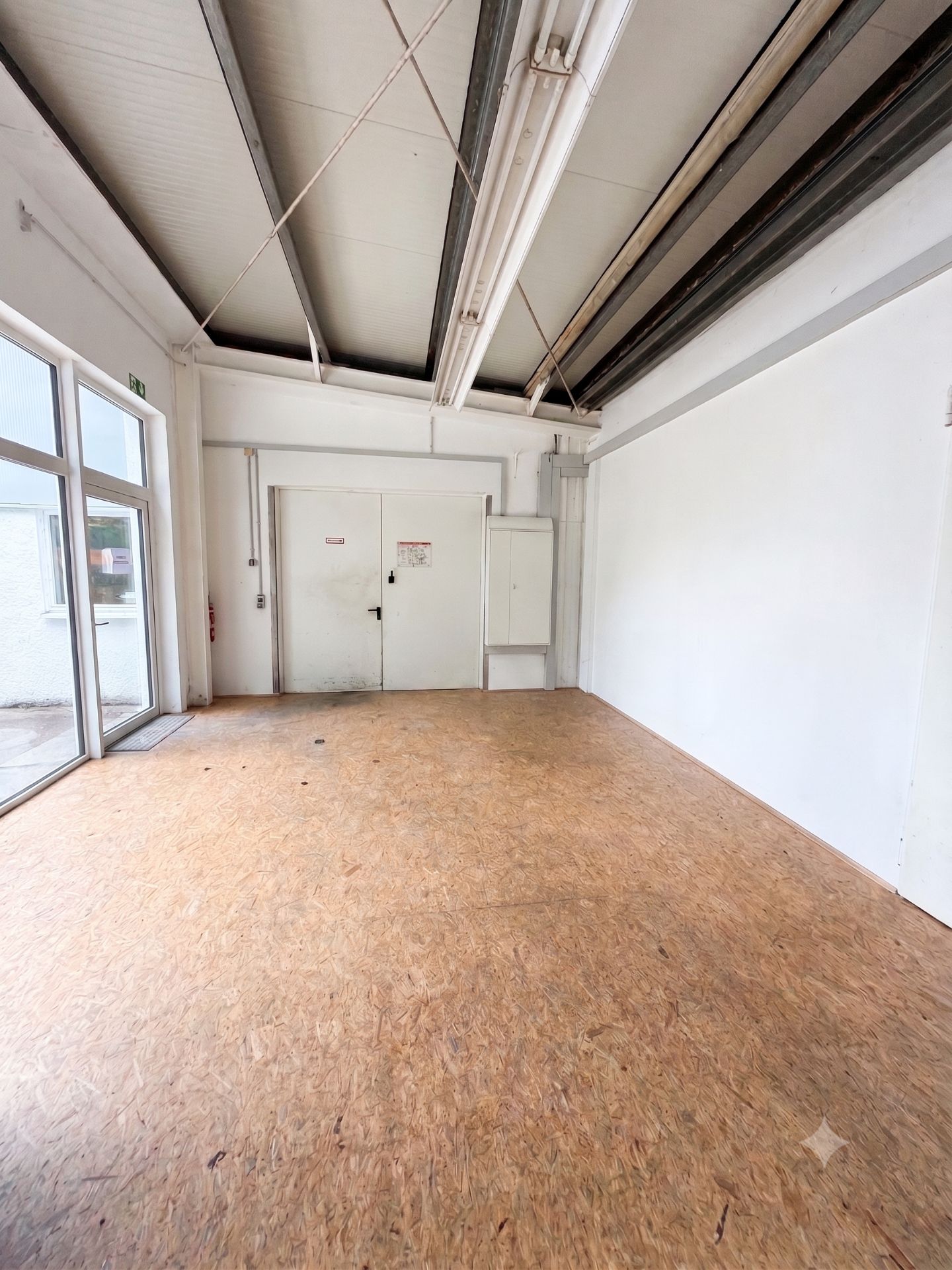 Leerer Raum mit Holzfußboden, weißen Wänden und Glastür.