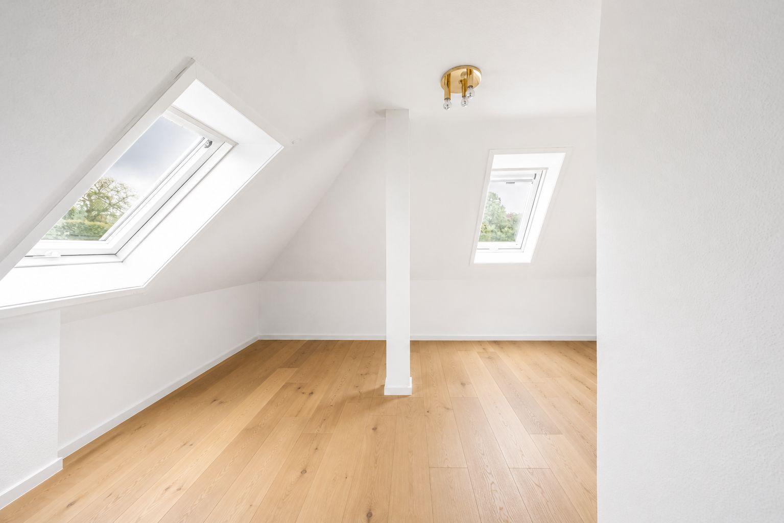 Heller Dachraum mit weißen Wänden, Holzfußboden und zwei Dachfenstern.