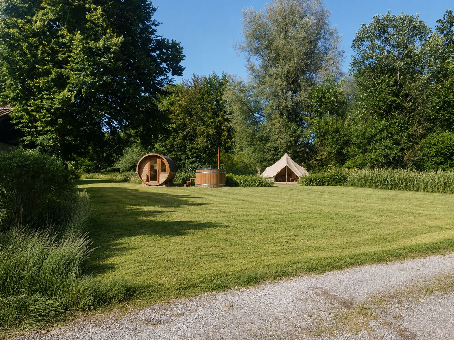 Großer grüner Rasen mit Holzhütte, Zelt und Bäumen im Hintergrund.