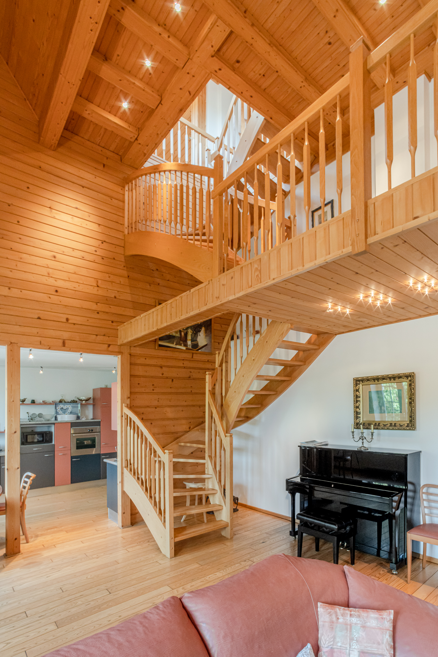 Wohnzimmer mit Holztreppe, offenem Dachstuhl und Klavier neben einer modernen Küche.