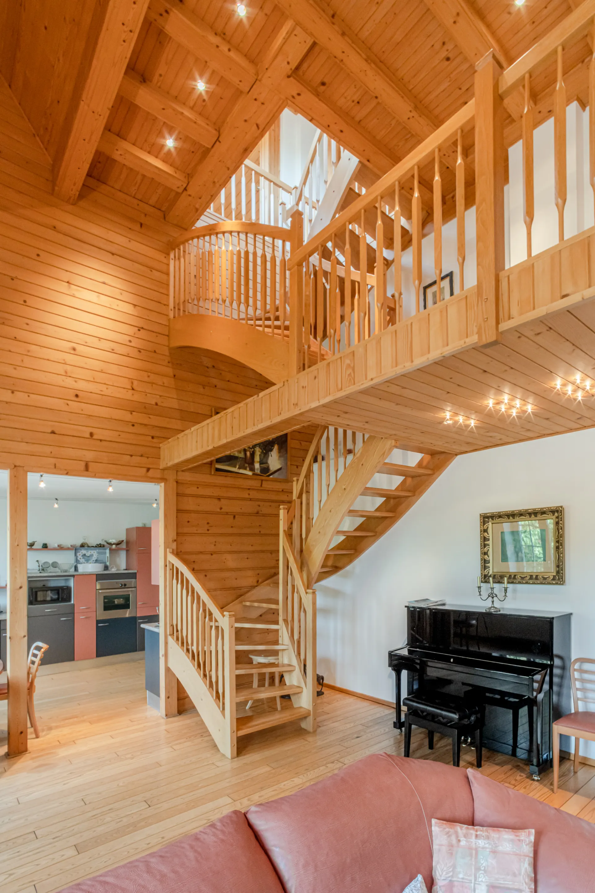 Wohnzimmer mit Holztreppe, offenem Dachstuhl und Klavier neben einer modernen Küche.