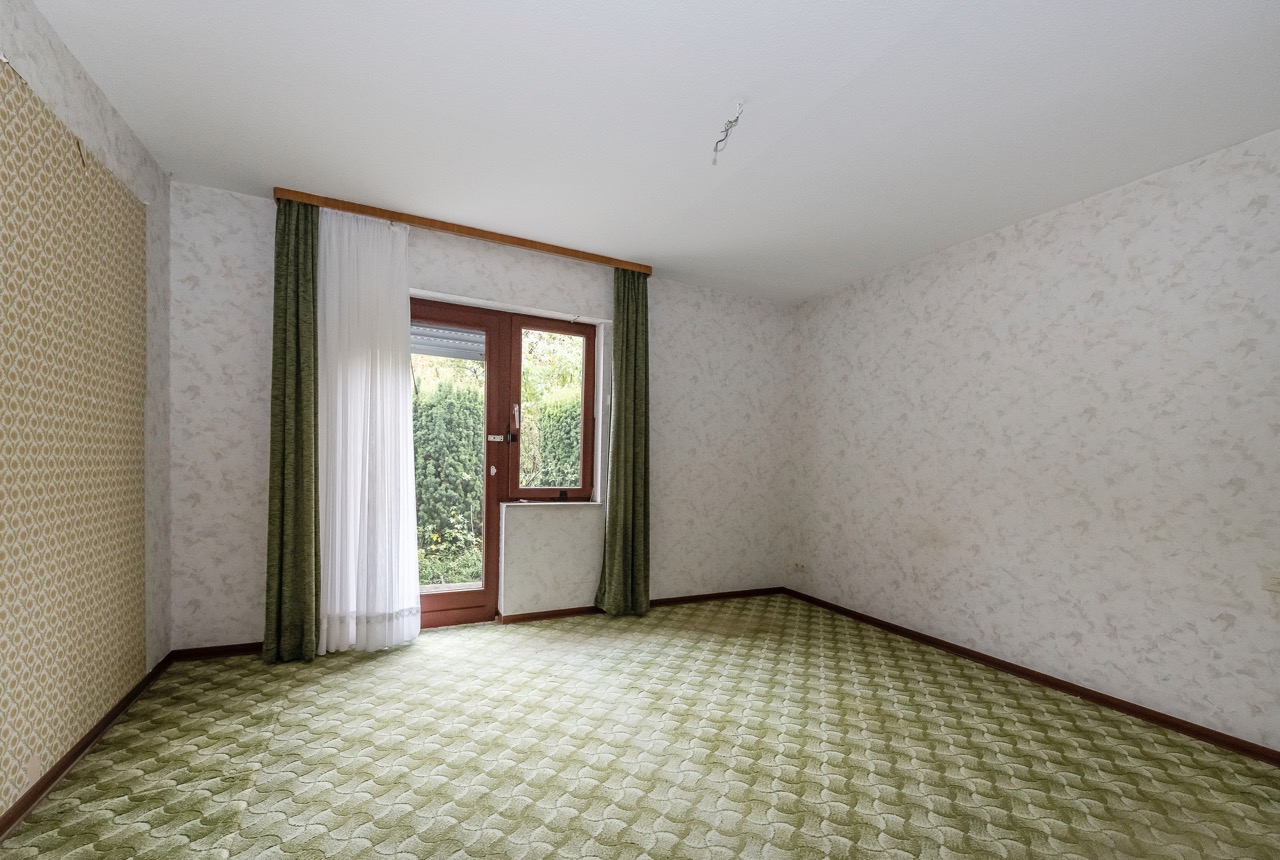 Leeres Zimmer mit gemustertem Teppich, Fenster und Tür mit grünen Vorhängen.