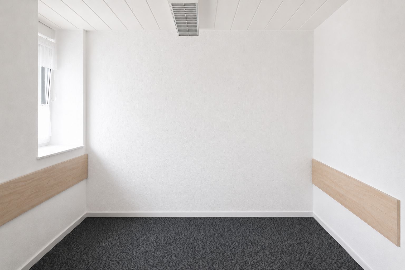 Leerer, heller Raum mit weißem Wänden, dunklem Teppich und Holzpaneelen an den Seiten.