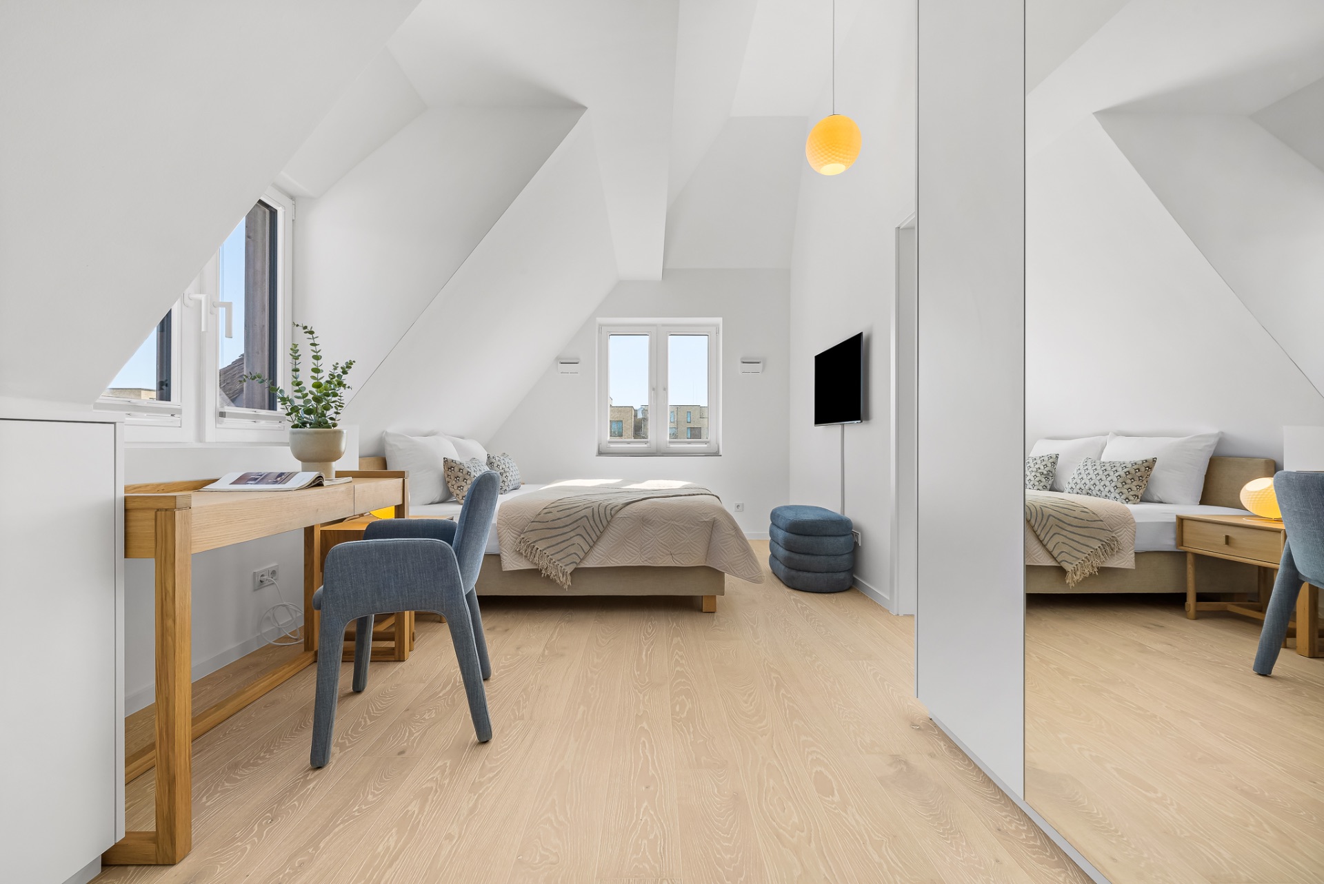 Helles Schlafzimmer mit Schreibtisch, Doppelbett und Dachschrägen, großes Fenster und Spiegel.