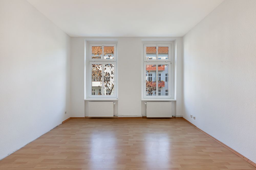 Leerer, heller Raum mit zwei großen Fenstern und hellem Holzboden.