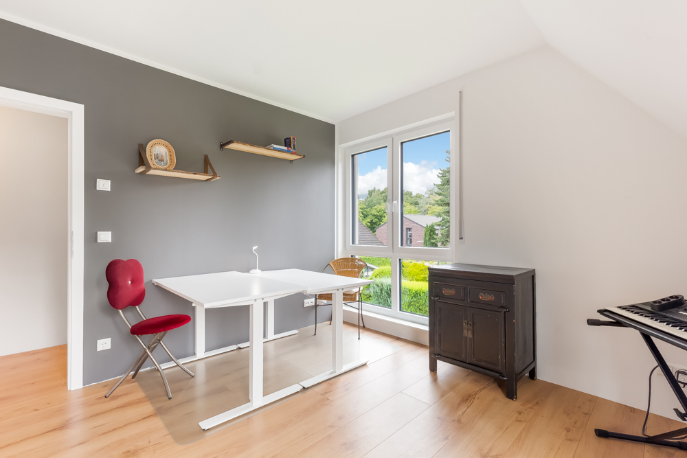 Helles Arbeitszimmer mit Schreibtisch, Stuhl, Kommode, großen Fenstern und Keyboard.