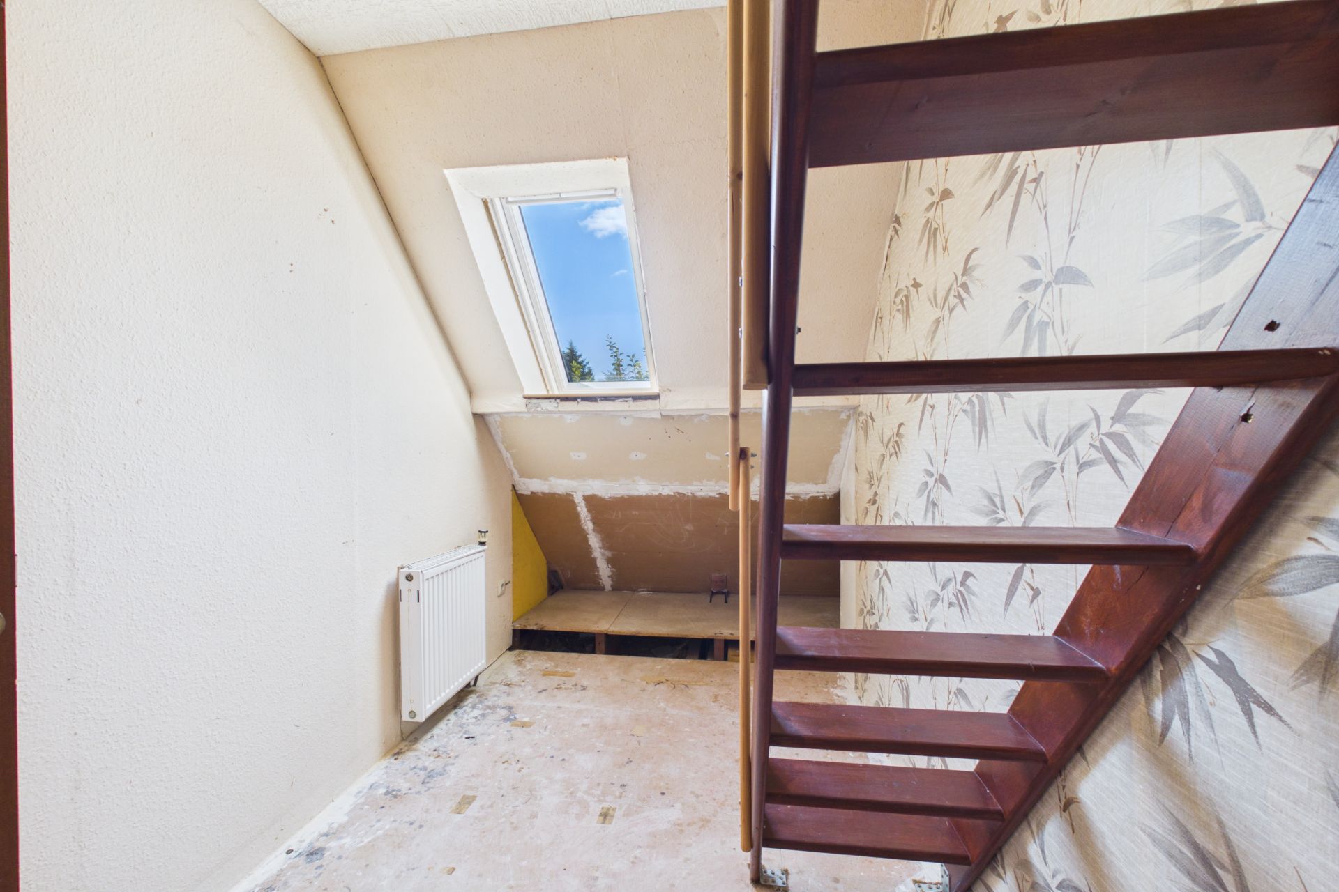 Kleiner Raum mit Holztreppe, Dachfenster und Tapete mit Pflanzenmuster.