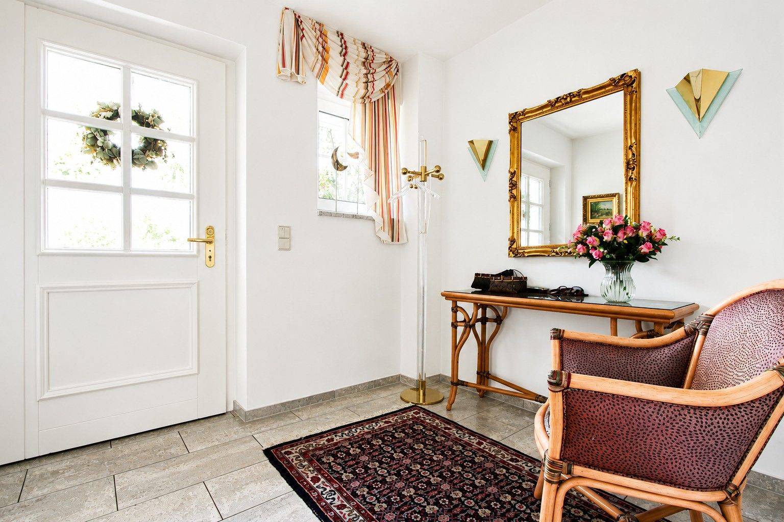 Heller Flur mit Teppich, Stuhl, Tisch mit Blumenvase und großem Spiegel an der Wand.