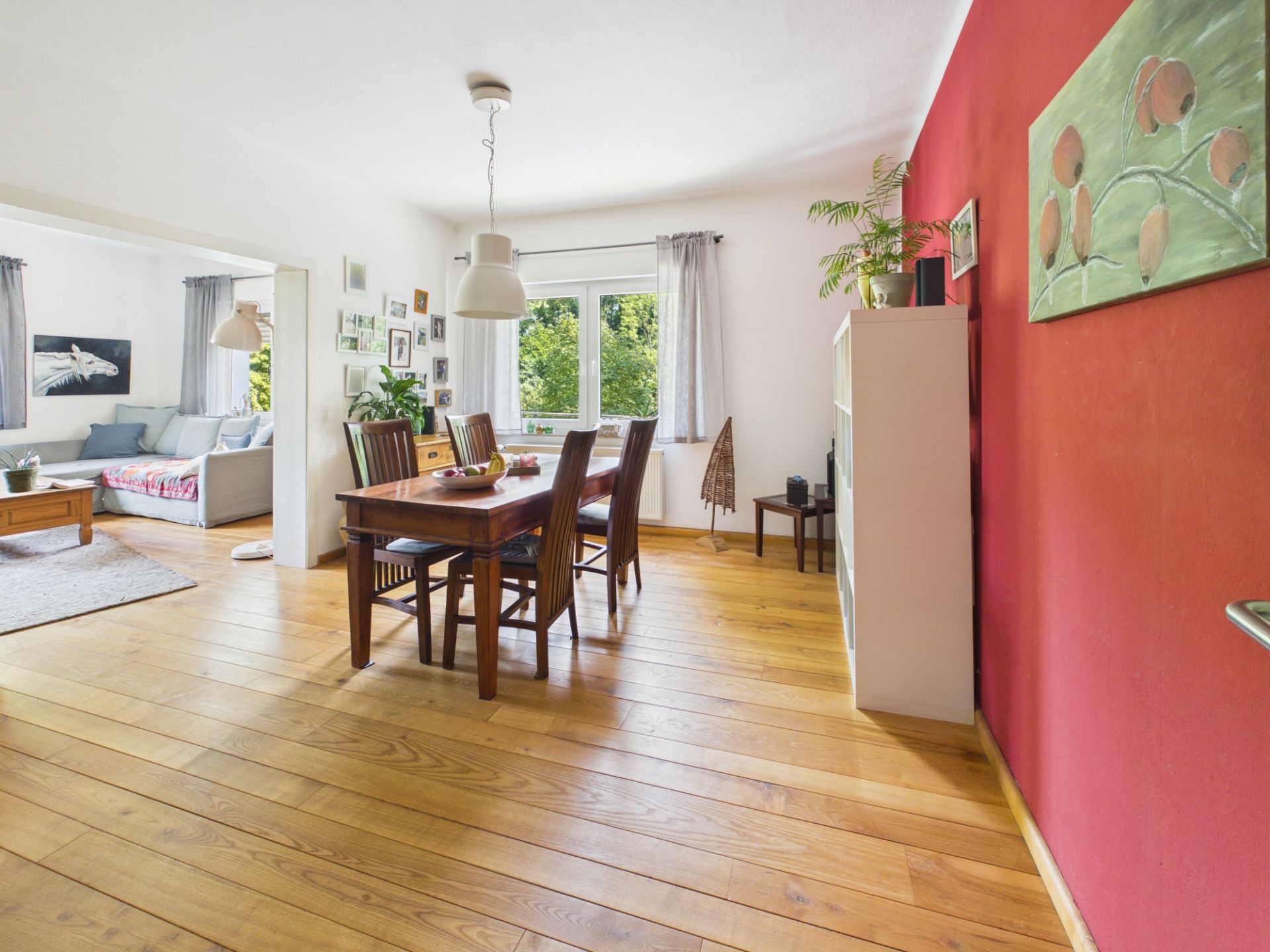 Esszimmer mit Holzboden, Holztisch, sechs Stühlen und angrenzendem Wohnzimmer mit Sofa.