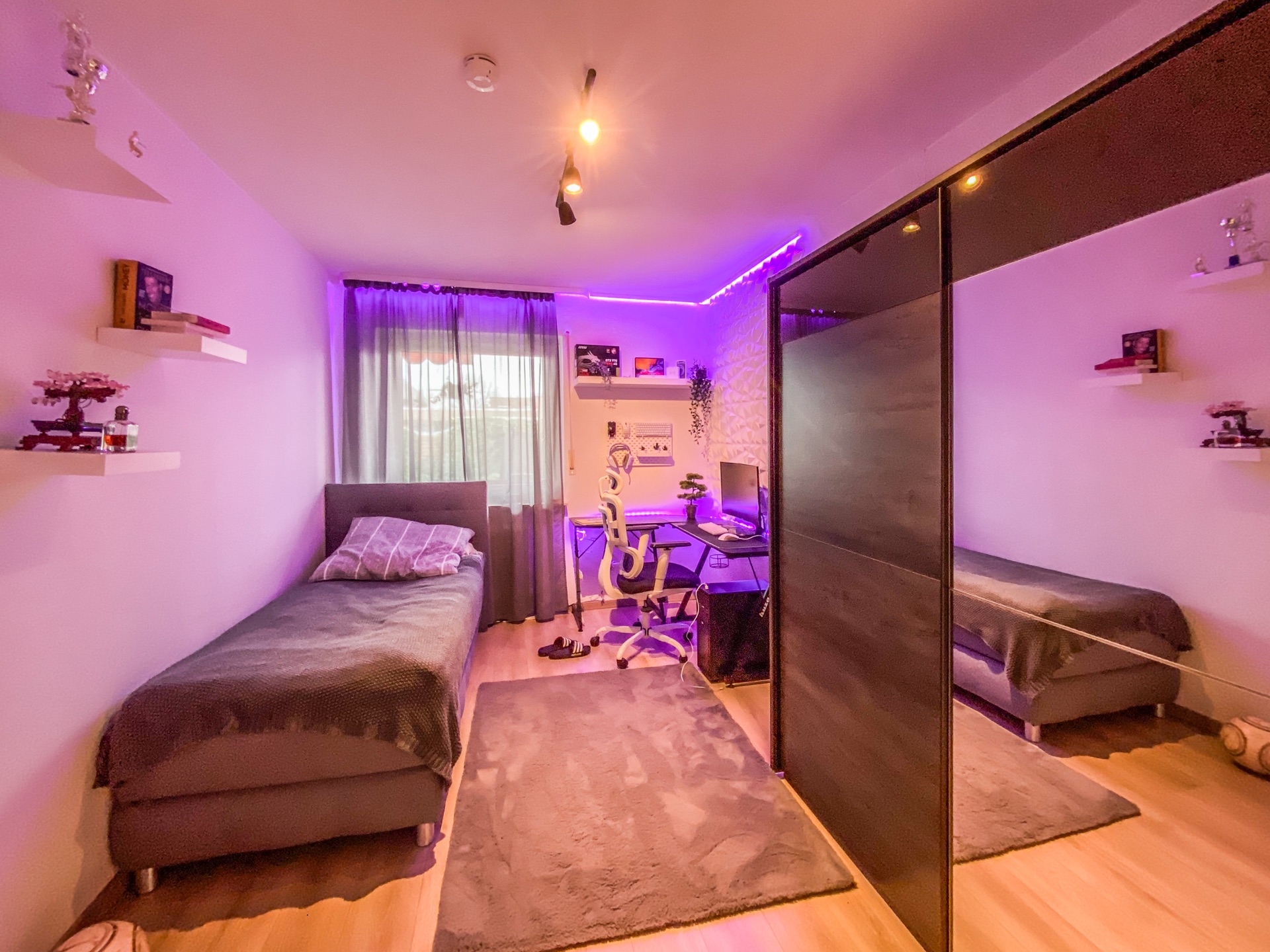 Modernes Schlafzimmer mit Bett, Schreibtisch, Computer und kleinem Kleiderschrank mit Spiegeltüren.
