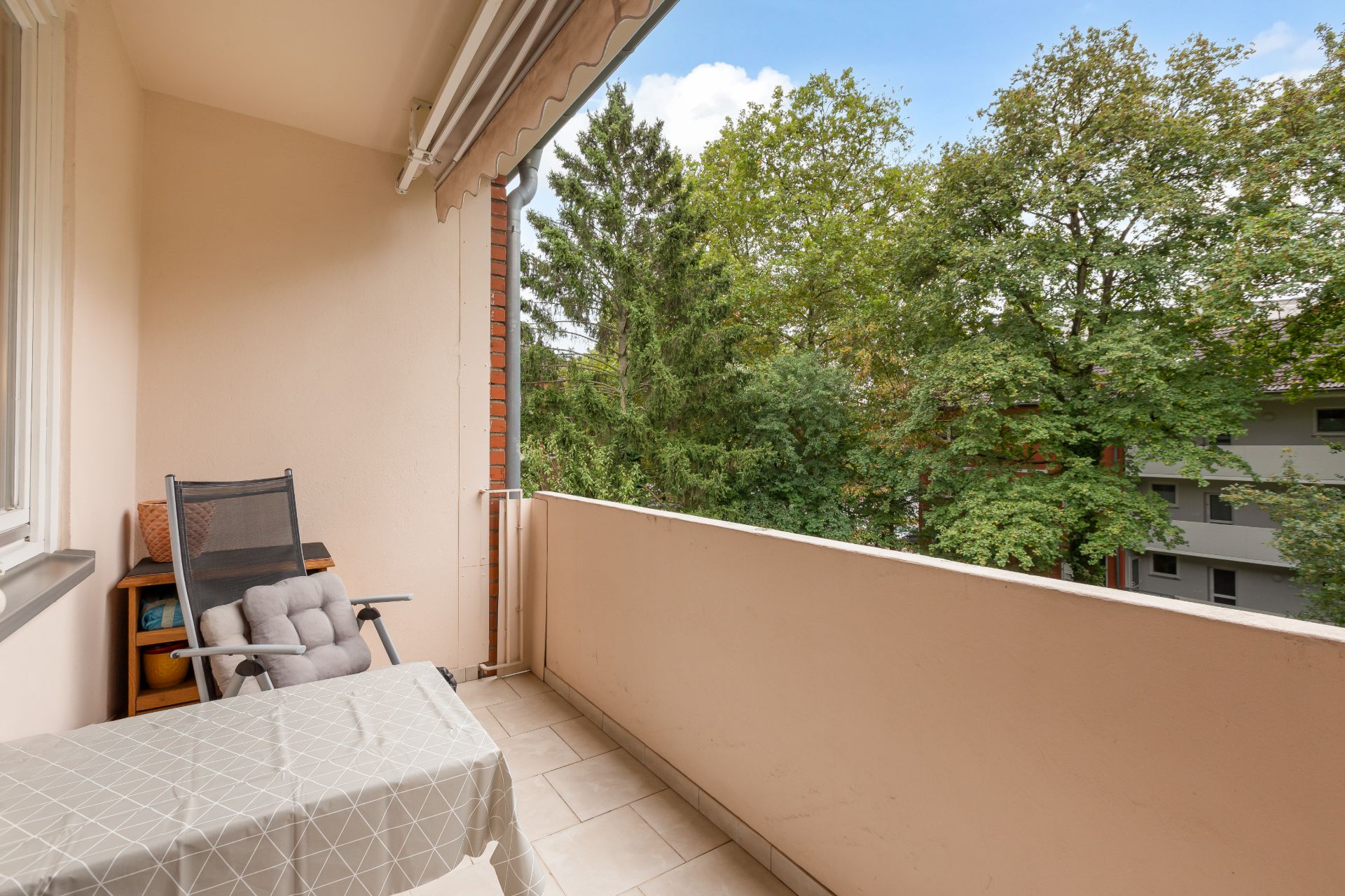 Balkon mit Tisch, Stuhl und Blick auf grüne Bäume.
