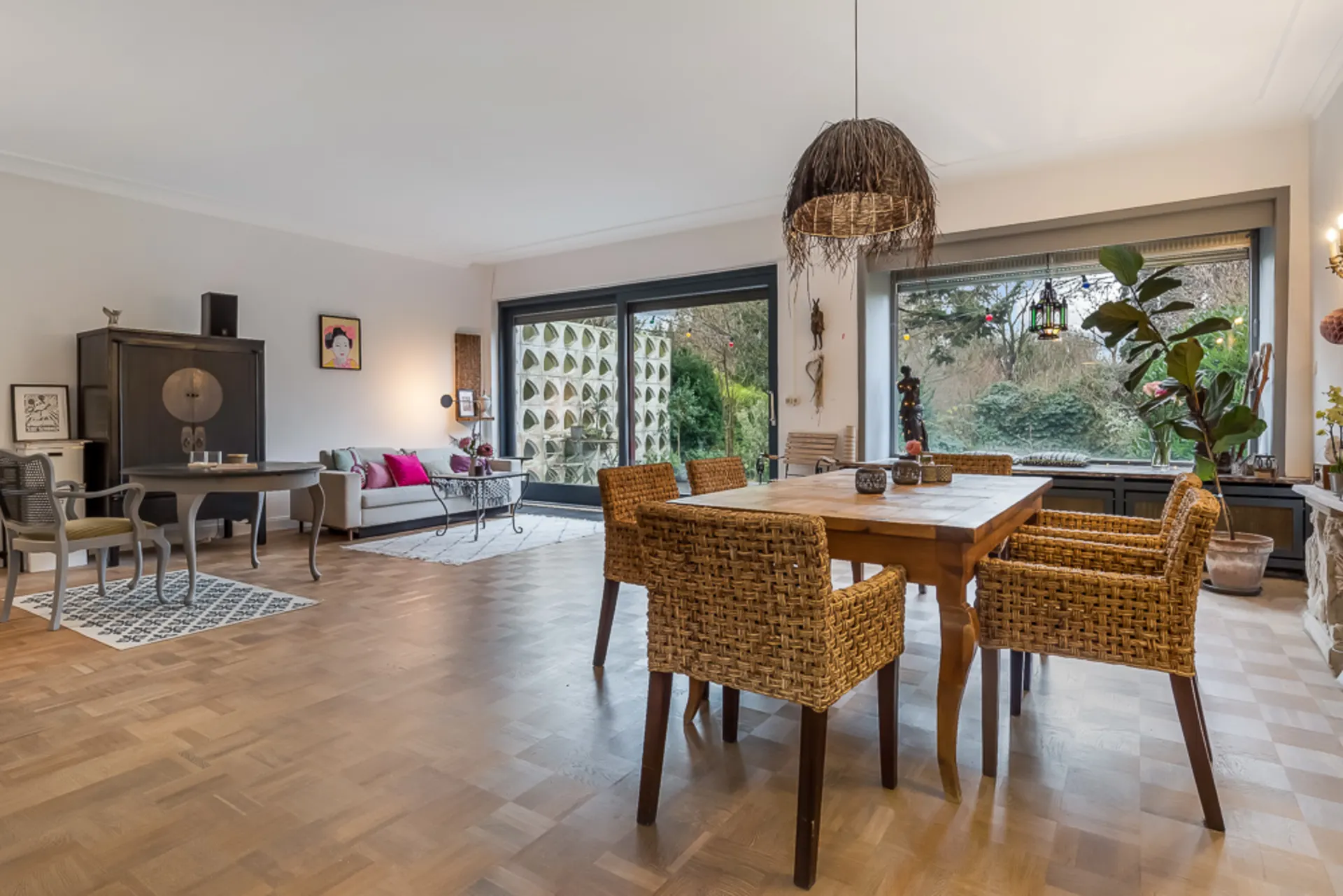 Heller Wohn- und Essbereich mit Holztisch, geflochtenen Stühlen und großen Fenstern zum Garten.
