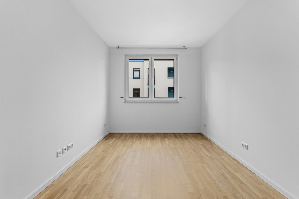 Leerer, heller Raum mit Holzfußboden und einem Fenster in der Mitte der Rückwand.