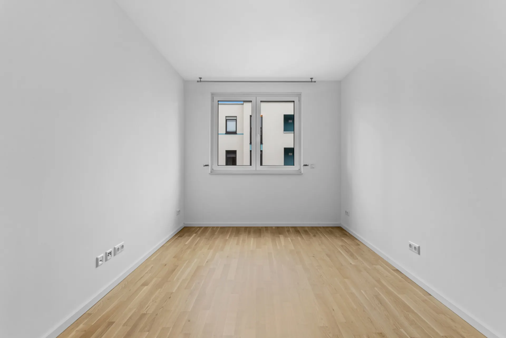 Leerer, heller Raum mit Holzfußboden und einem Fenster in der Mitte der Rückwand.