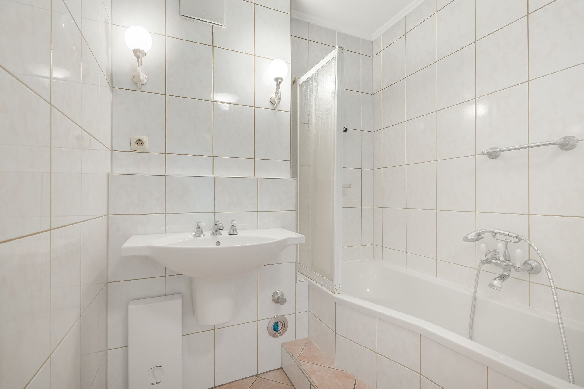 Helles Badezimmer mit Waschbecken, Spiegel, Badewanne und zwei Wandleuchten.