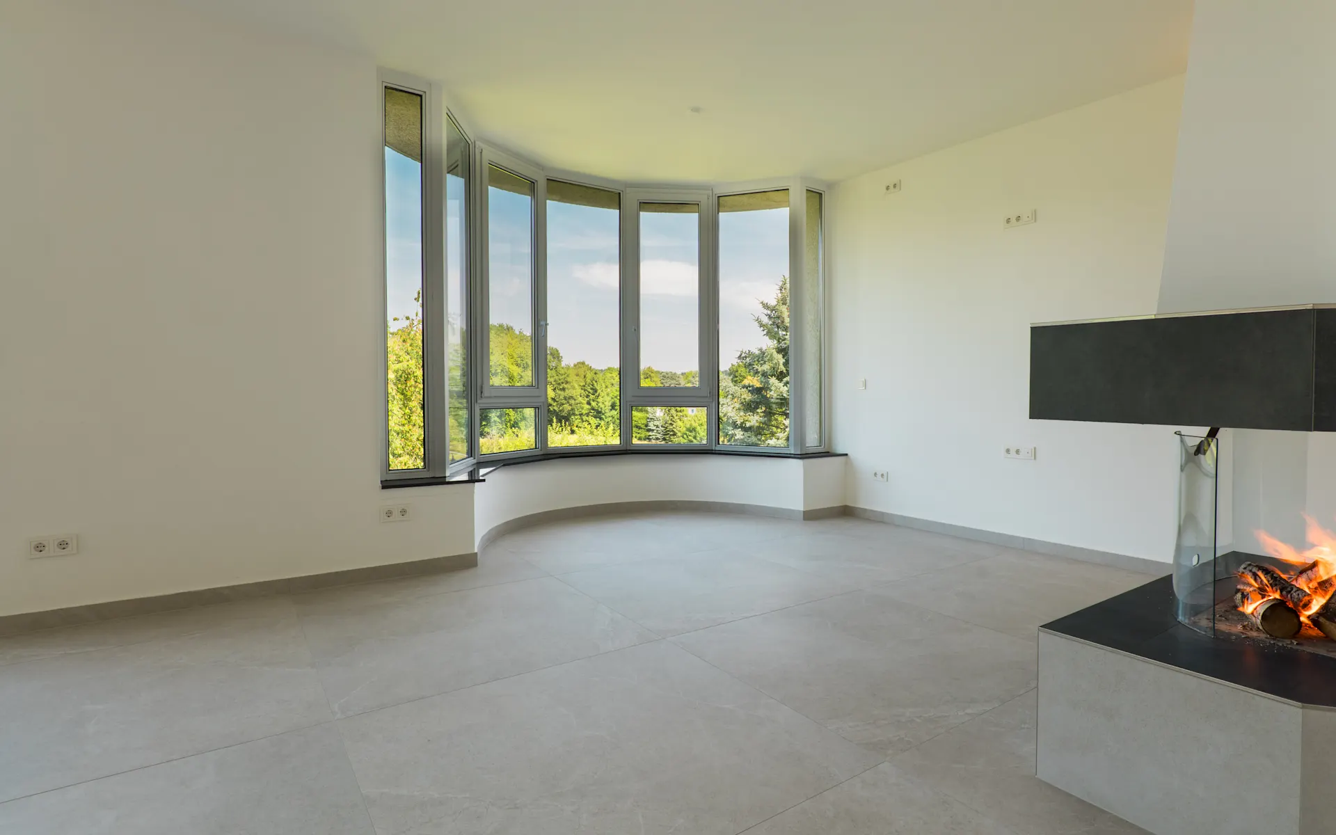 Helles Wohnzimmer mit großen Fenstern und modernem Kamin auf der rechten Seite.