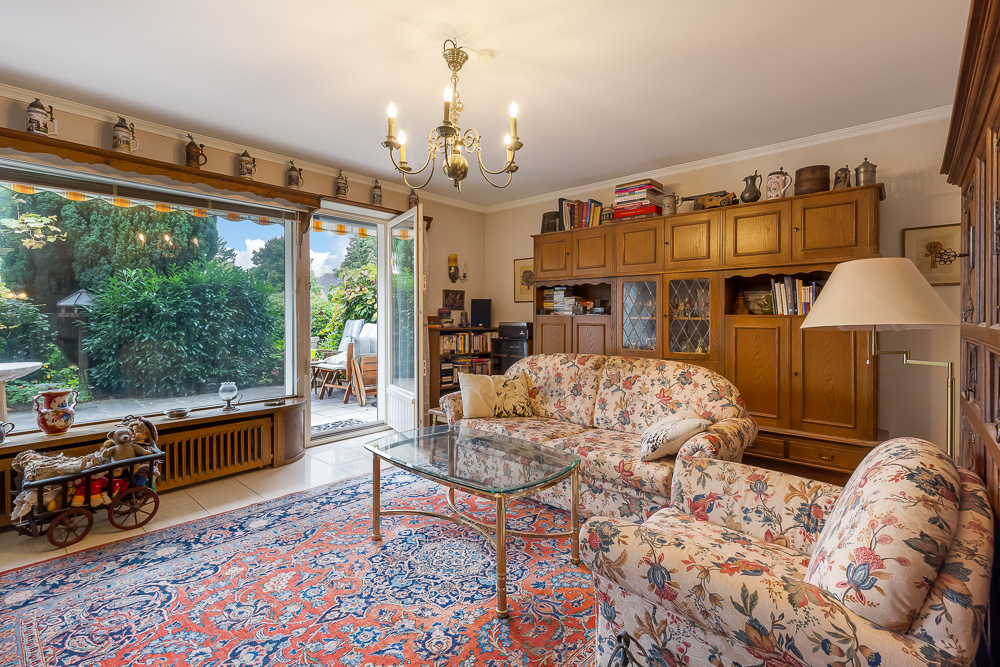 Wohnzimmer mit Blümchen-Sofas, Glastisch, großem Fenster zum Garten und Holzmöbeln.