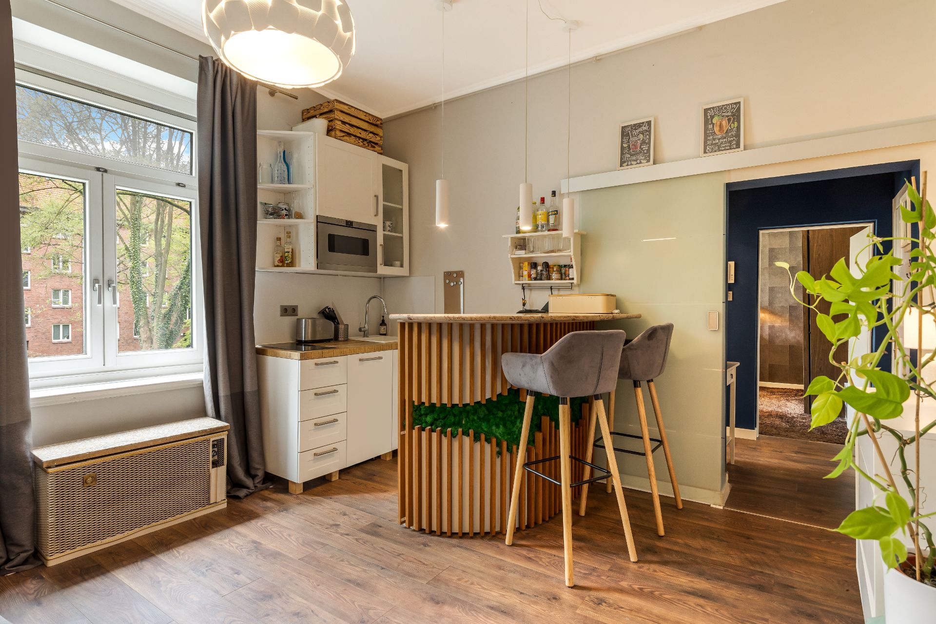 Moderne kleine Küche mit Bartresen, zwei Barhockern, einem Fenster und Holzfußboden.