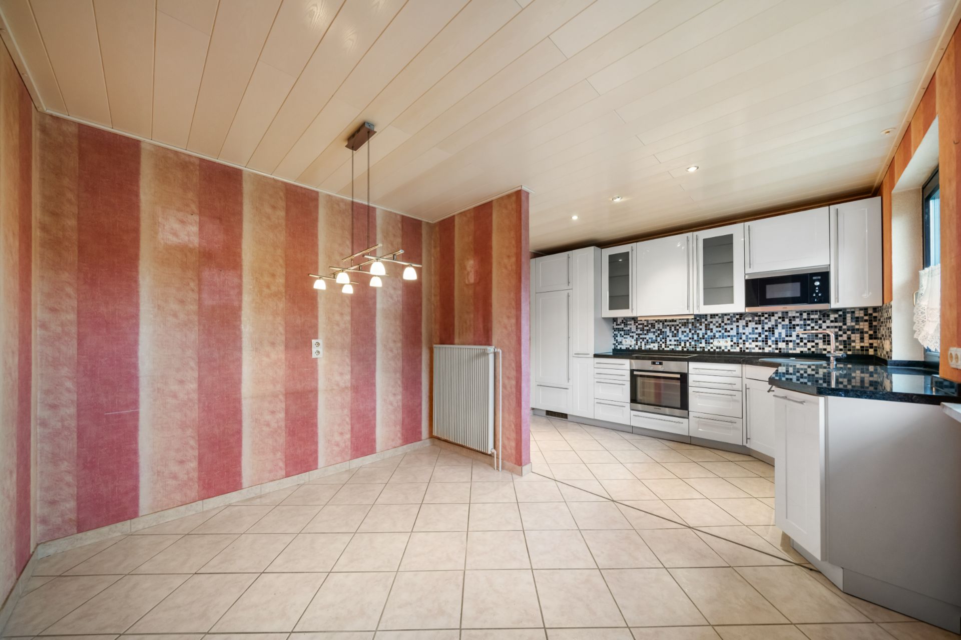 Moderne Küche mit weißen Schränken, Fliesenspiegel und angrenzendem Essbereich mit gestreifter Wand.