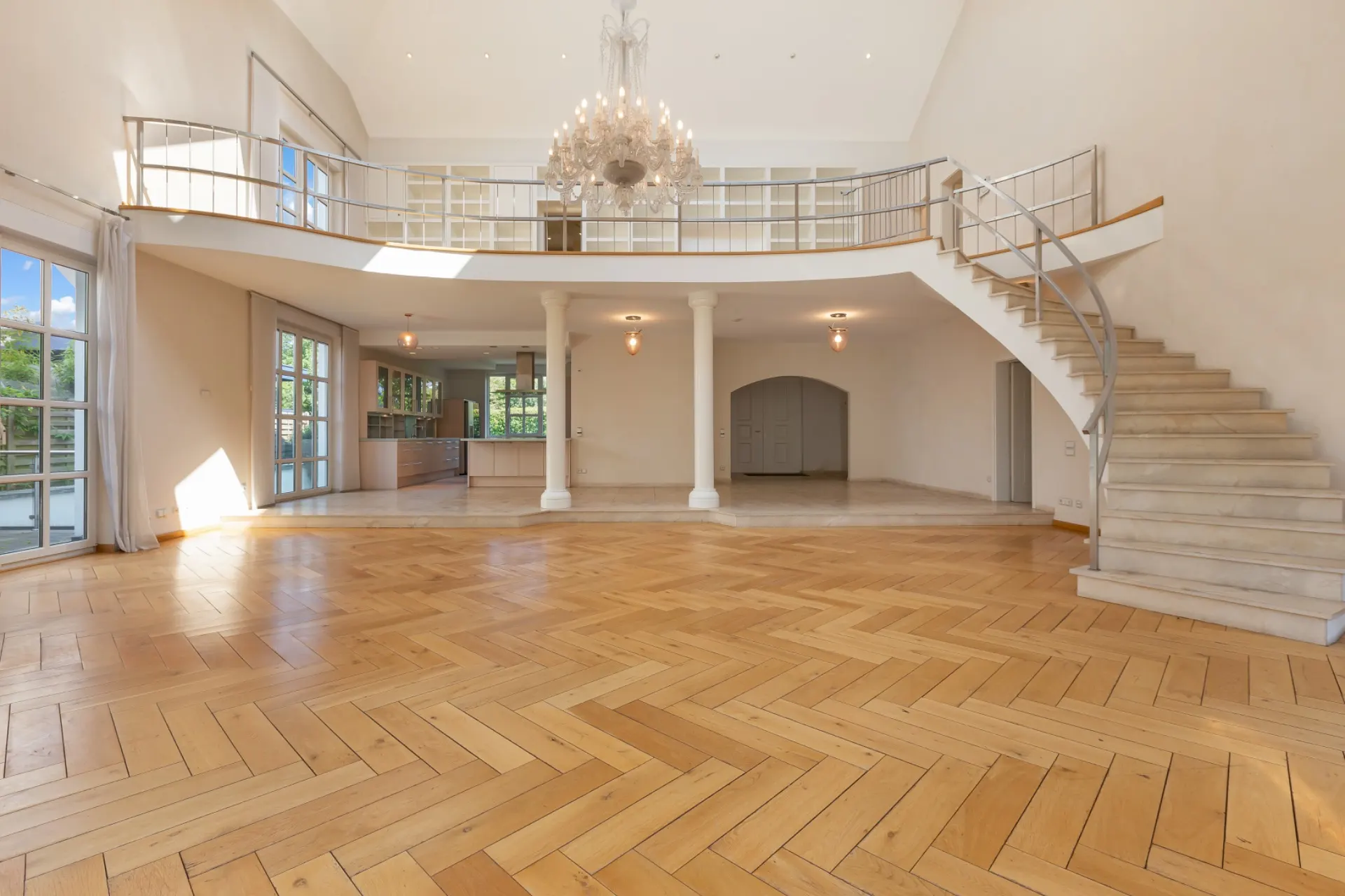 Großes, helles Wohnzimmer mit Parkettboden, Kronleuchter, offener Küche und Treppe zur Galerie.