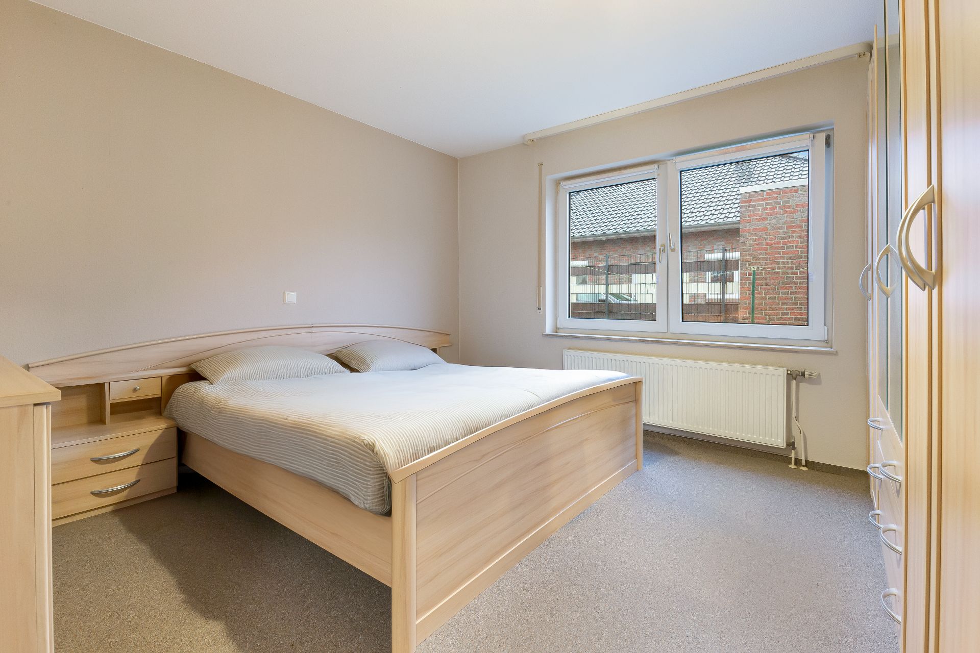 Helles Schlafzimmer mit Doppelbett, Nachttischen und großem Fenster.