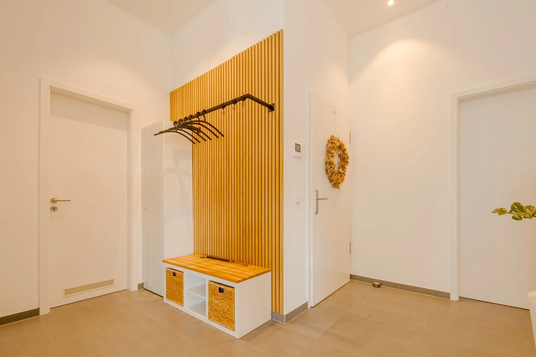 Heller Flur mit Garderobe aus Holz, Kleiderbügeln und zwei weißen Türen.