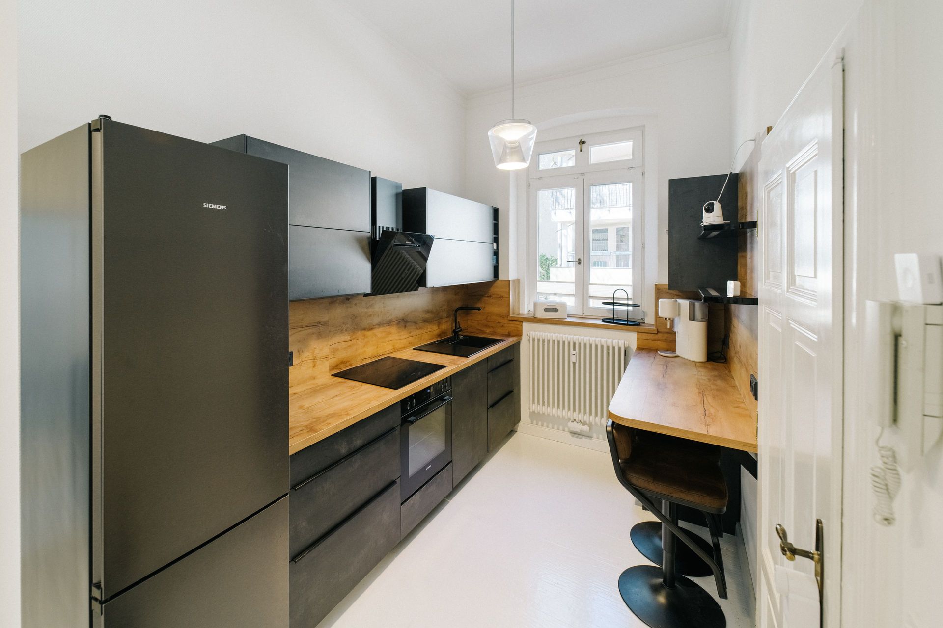 Moderne Küche mit schwarzen Schränken, Holzarbeitsplatte und kleinem Essbereich am Fenster.