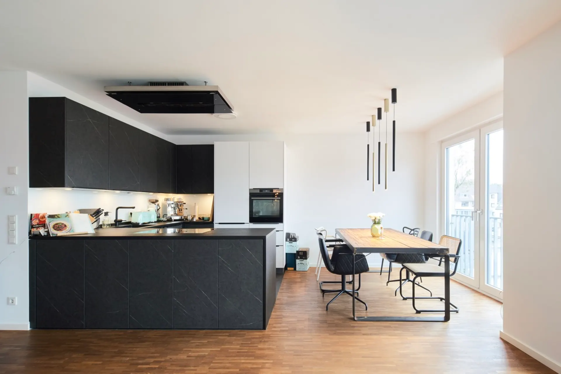 Moderne Küche mit dunklen Schränken, Essbereich mit Holztisch und Stühlen an großen Fenstern.