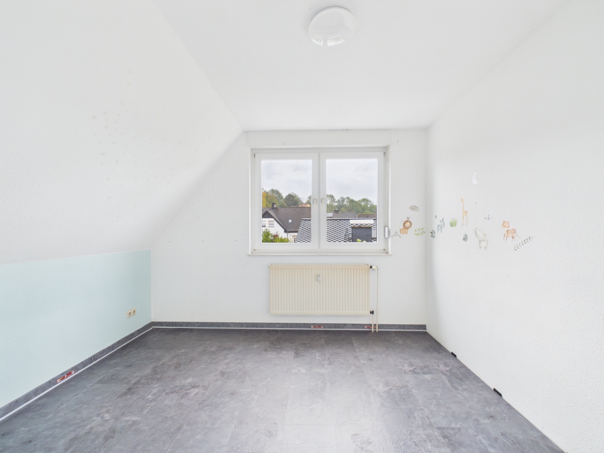 Leeres Zimmer mit grauem Boden, weißer Wand und Fenster, darunter ein Heizkörper.