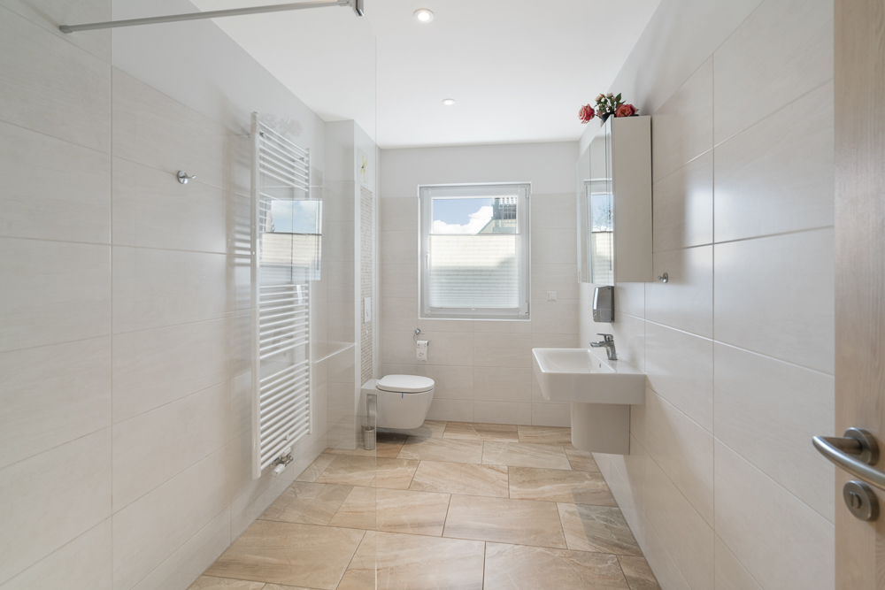 Helles, modernes Badezimmer mit großem Fenster, Waschbecken, WC und Handtuchheizkörper.