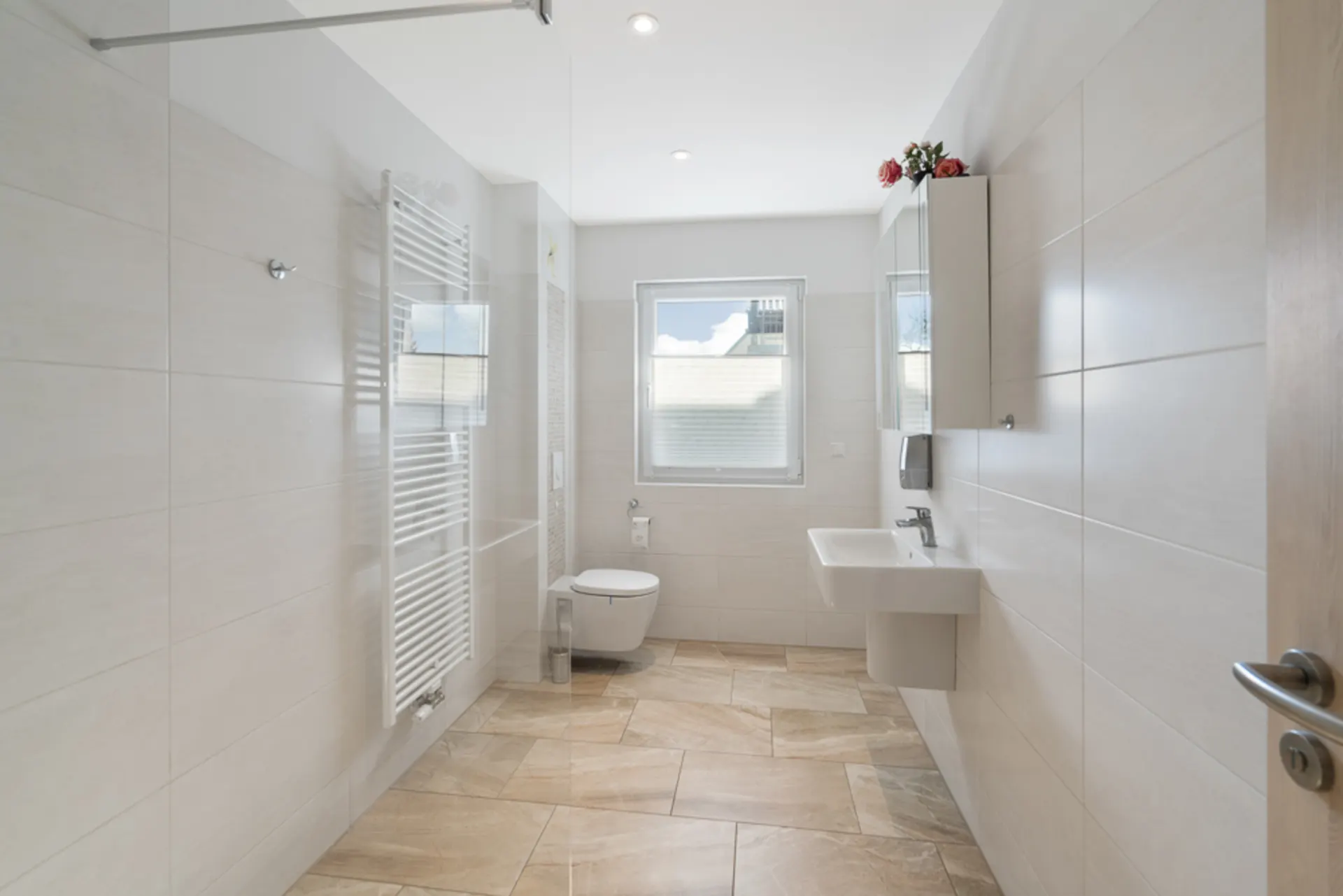Helles, modernes Badezimmer mit großem Fenster, Waschbecken, WC und Handtuchheizkörper.