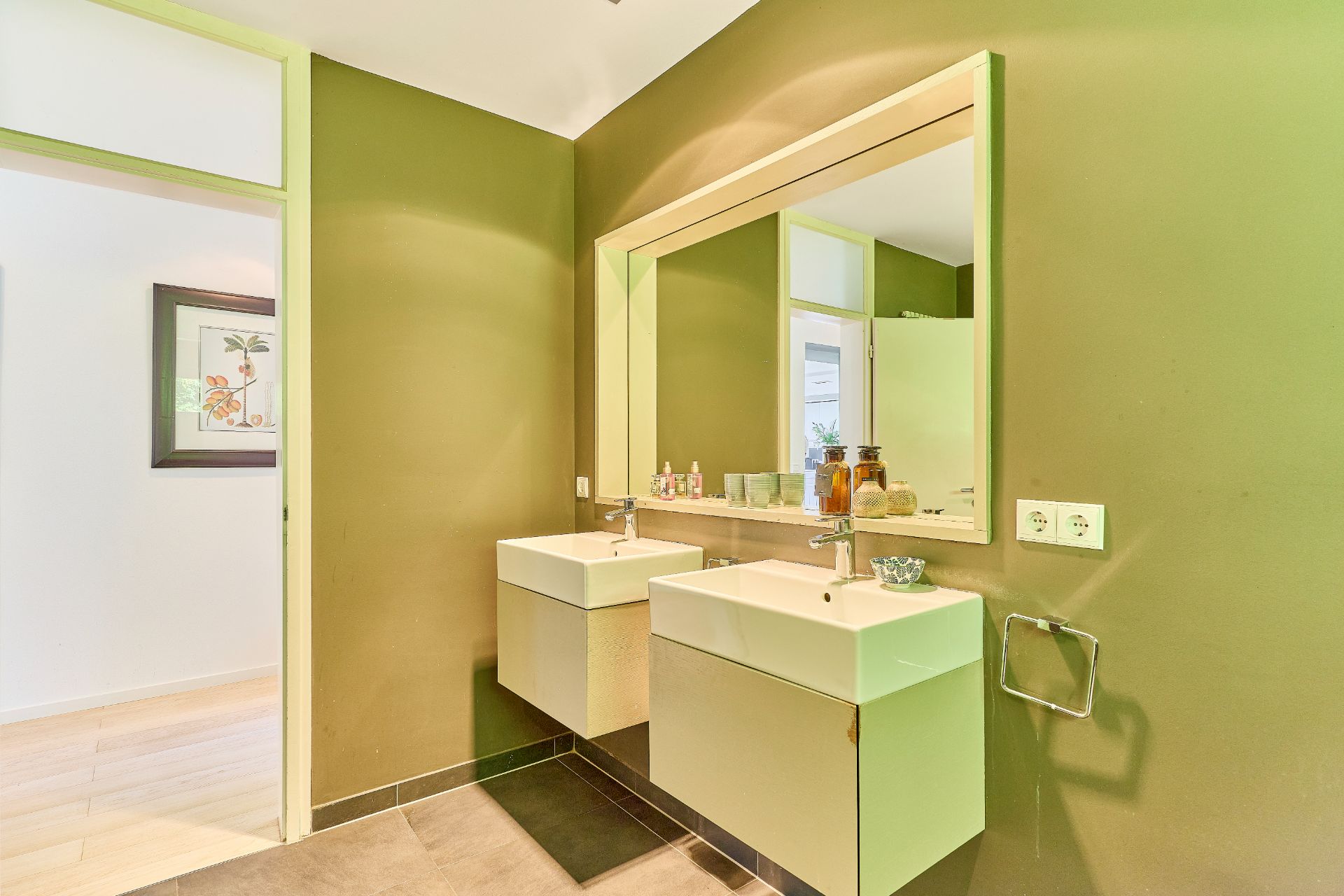 Modernes Badezimmer mit zwei Waschbecken, großem Spiegel und grünen Wänden.