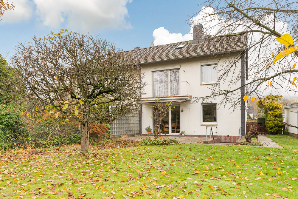 Zweistöckiges Wohnhaus mit Garten, herbstliche Bäume und Rasenfläche im Vordergrund.